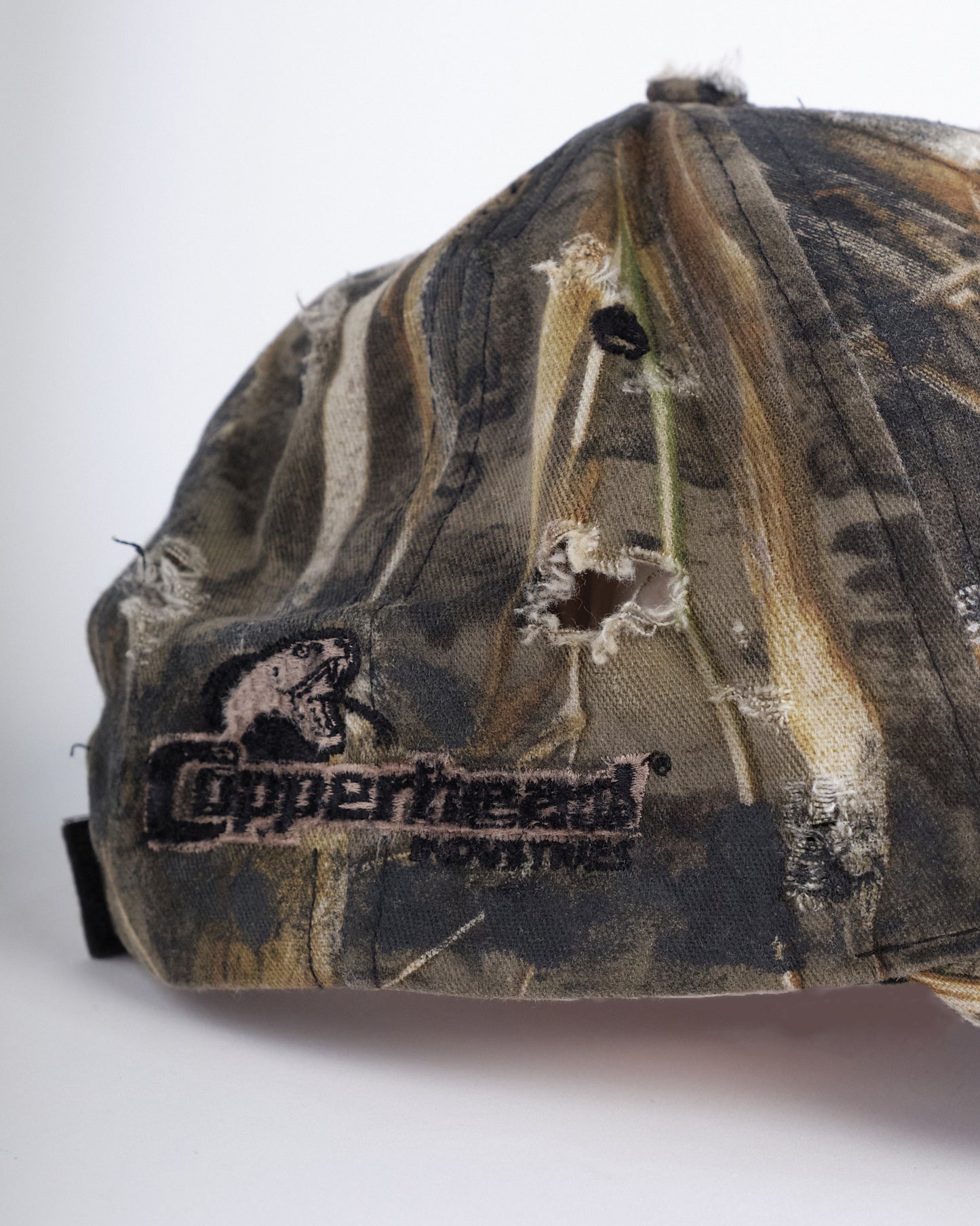 Back detail of ASTROBOI* DSG brown camouflage hat with rhinestone logo, black paint, clear resin accents, and stainless steel piercings, adjustable fit, handmade in NYC.