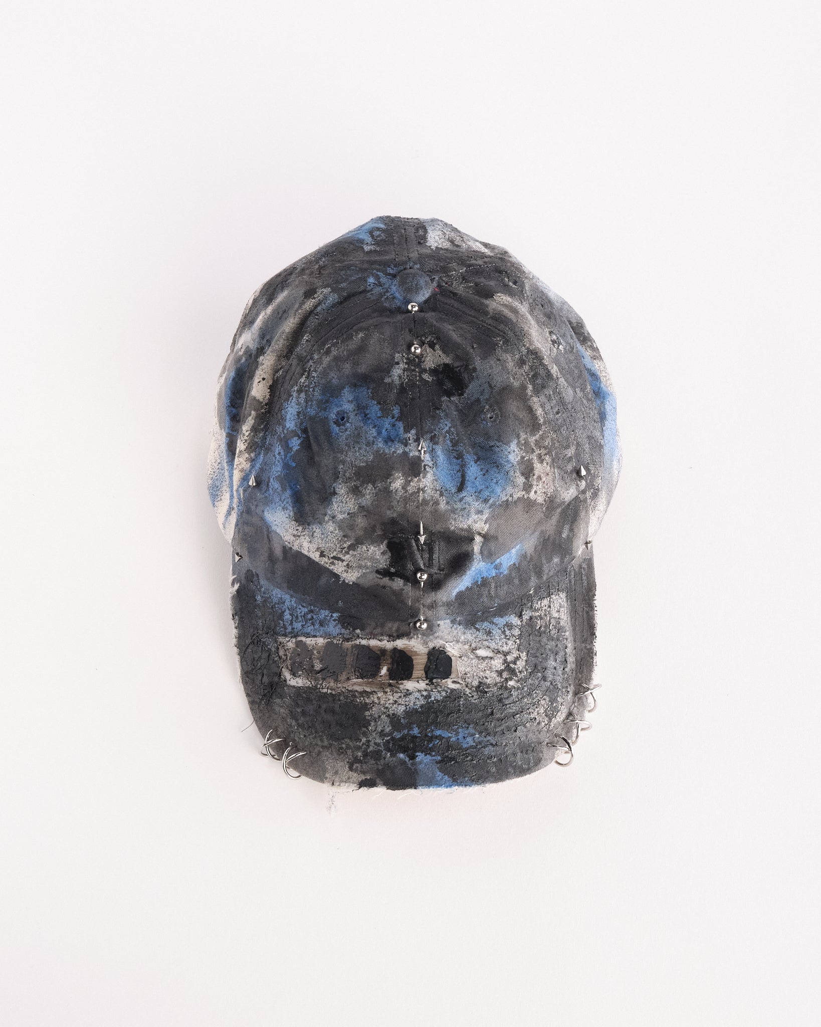 Overview of Black Vuori baseball hat customized by ASTROBOI* with blue and black painted details, stainless steel piercings, and an embroidered V logo.