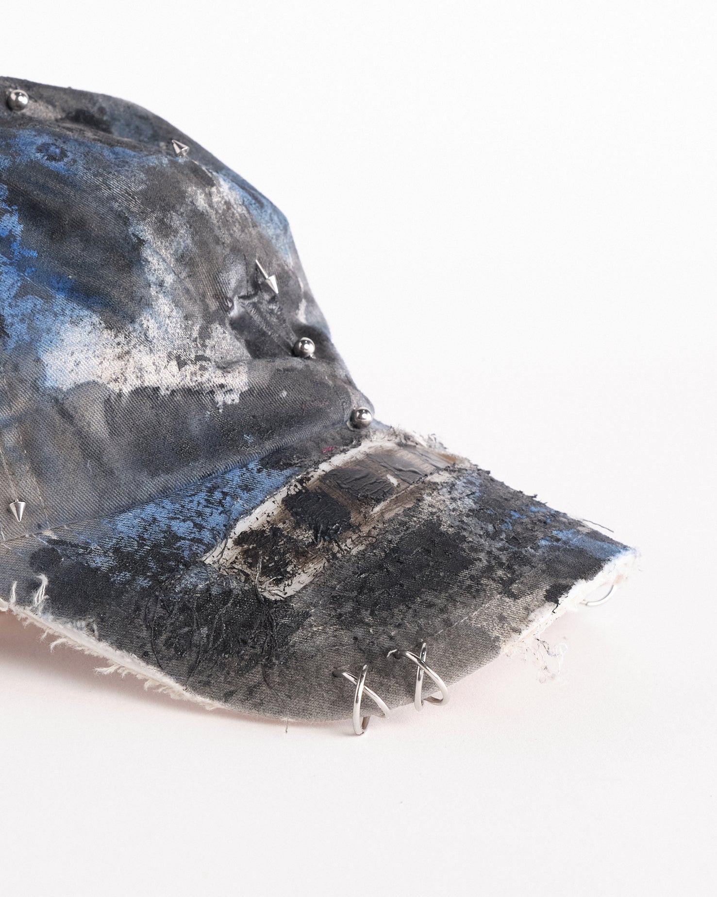 Front right detail of of Black Vuori baseball hat customized by ASTROBOI* with blue and black painted details, stainless steel piercings, and an embroidered V logo.