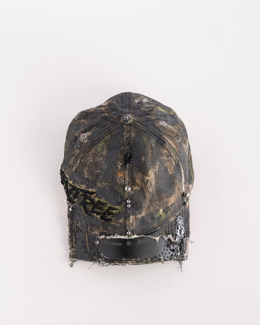 Top of Brown RealTree distressed half-visor hat with elastic base, black resin detailing, and a sawed-off visor for a deconstructed Y2K aesthetic.