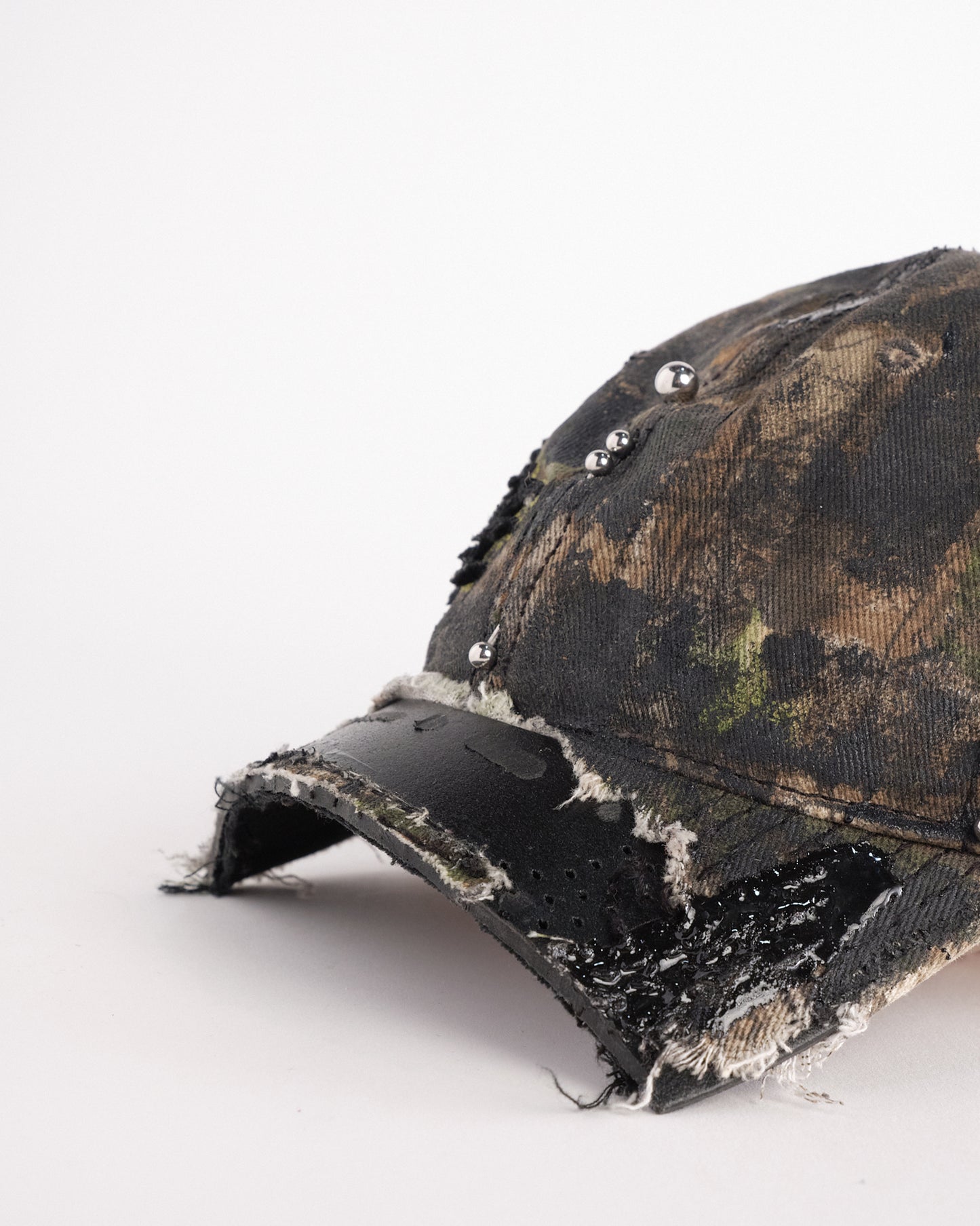 Left visor detail of Brown RealTree distressed half-visor hat with elastic base, black resin detailing, and a sawed-off visor for a deconstructed Y2K aesthetic.