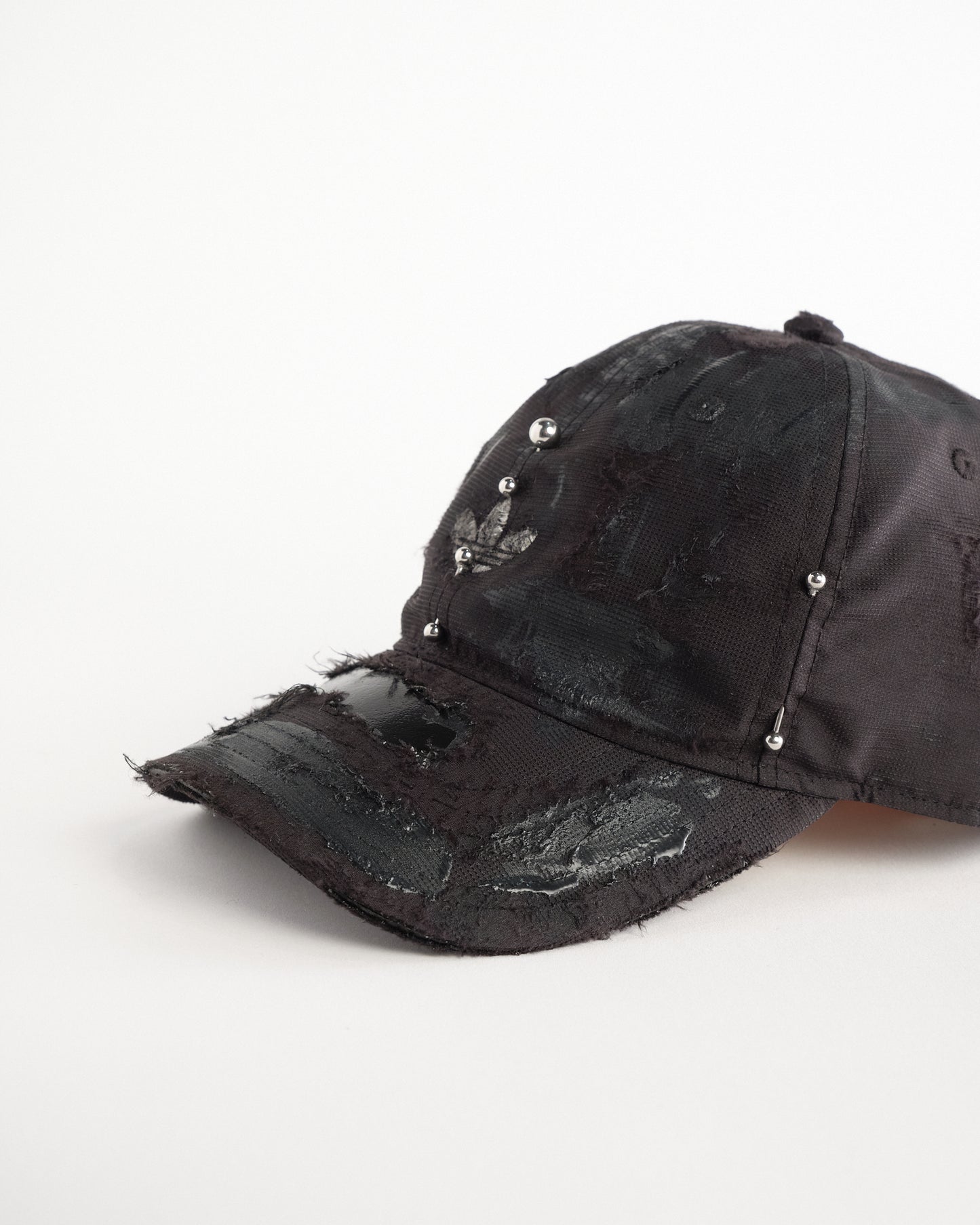 Detail of left side of Black Adidas hat customized by ASTROBOI* with distressing, black painted accents, and stainless steel piercings.