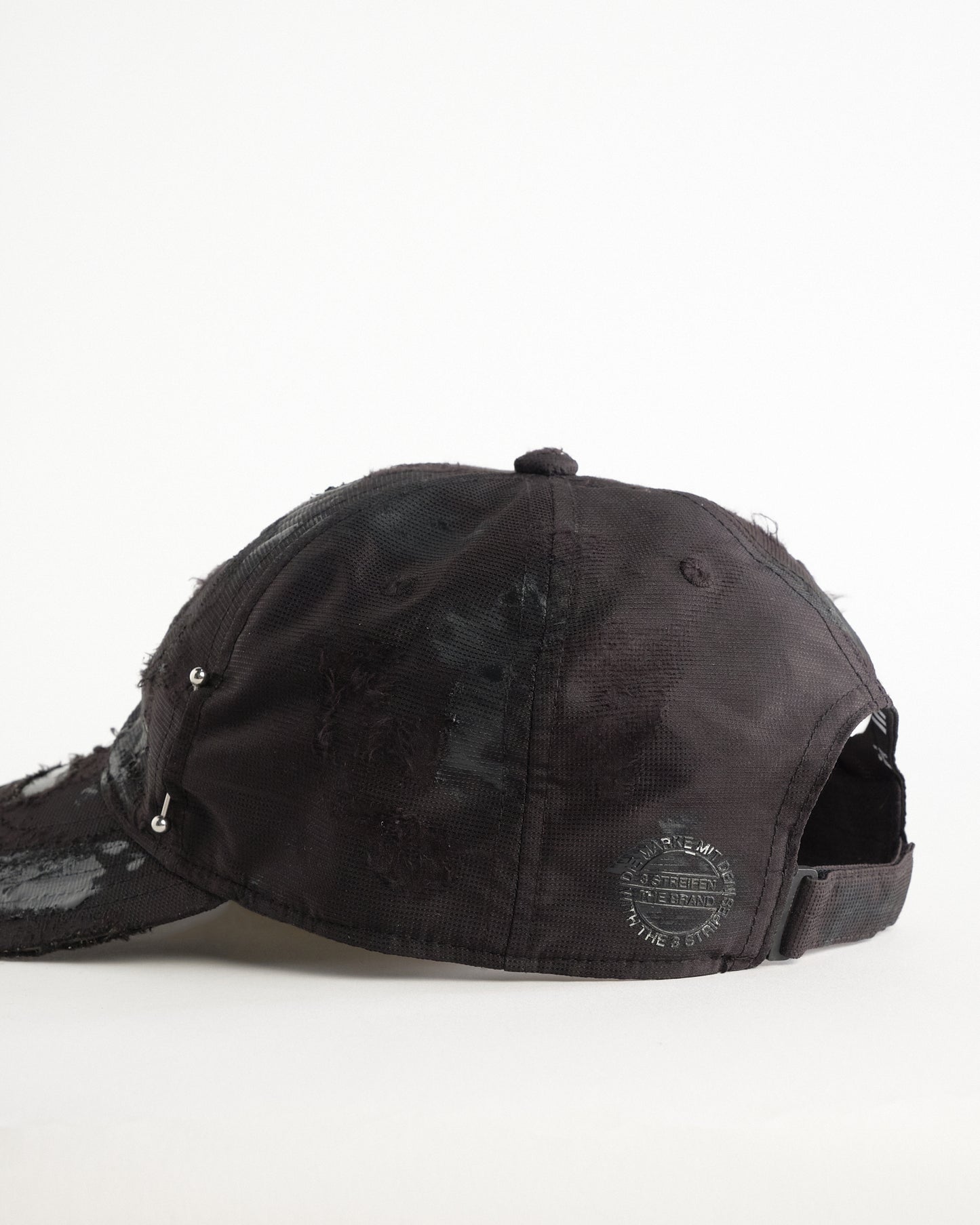 Back left detail of Black Adidas hat customized by ASTROBOI* with distressing, black painted accents, and stainless steel piercings.