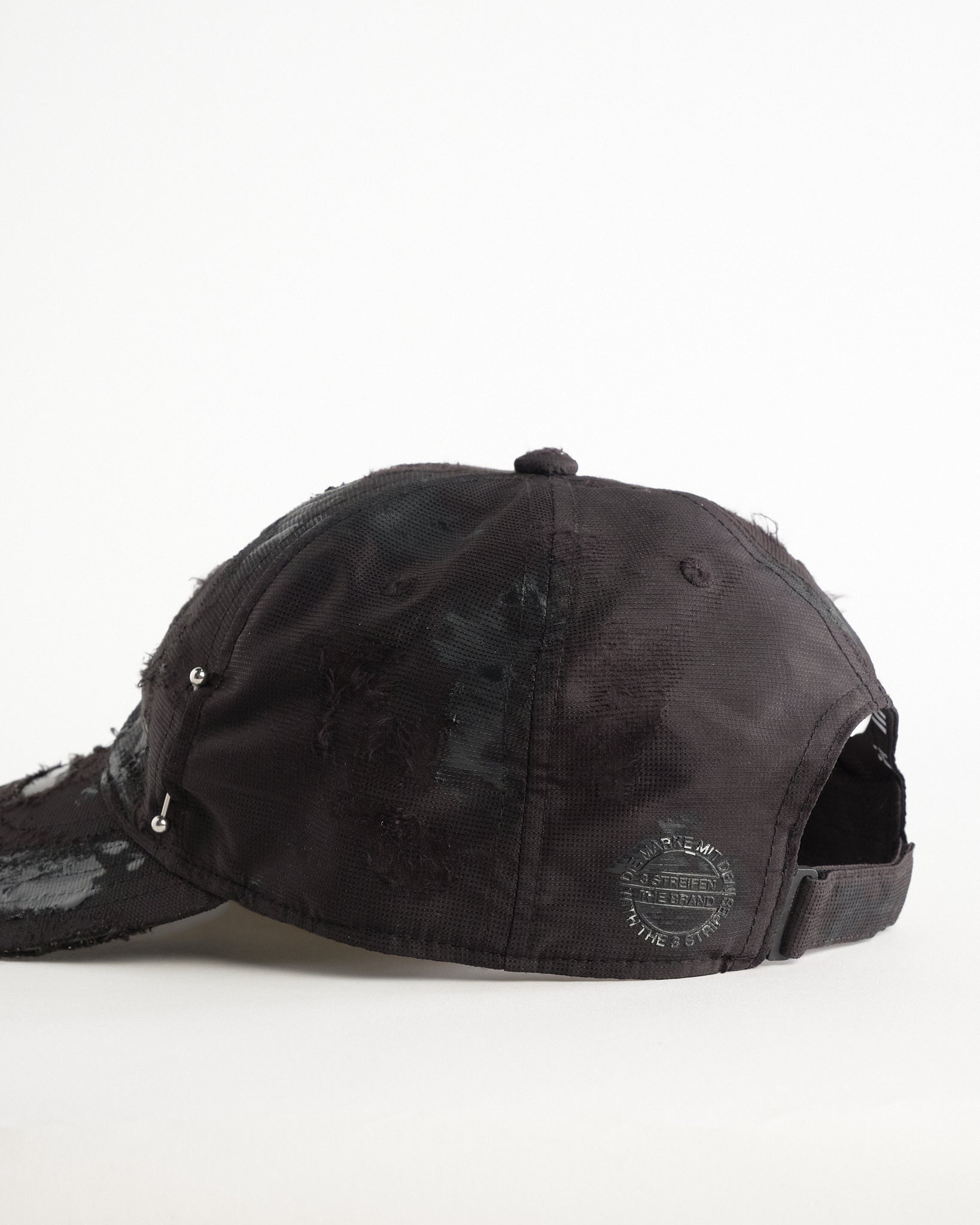 Back left detail of Black Adidas hat customized by ASTROBOI* with distressing, black painted accents, and stainless steel piercings.