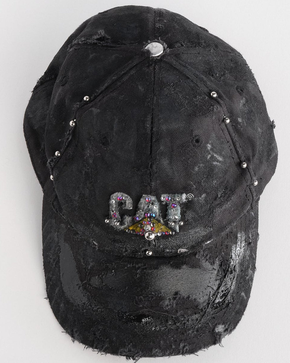 Top of ASTROBOI* x CAT black distressed pierced hat with rhinestone logo, resin and paint detailing, deconstructed visor, adjustable strap, handmade in NYC.