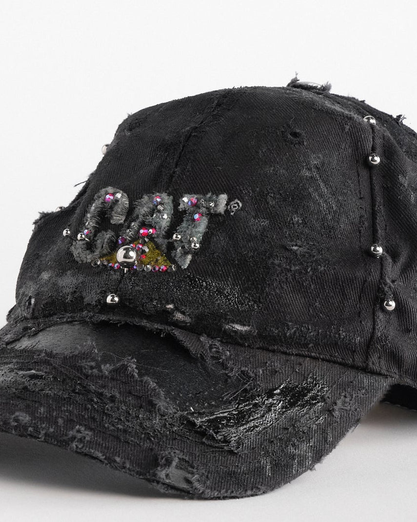 Front left detail of ASTROBOI* x CAT black distressed pierced hat with rhinestone logo, resin and paint detailing, deconstructed visor, adjustable strap, handmade in NYC.