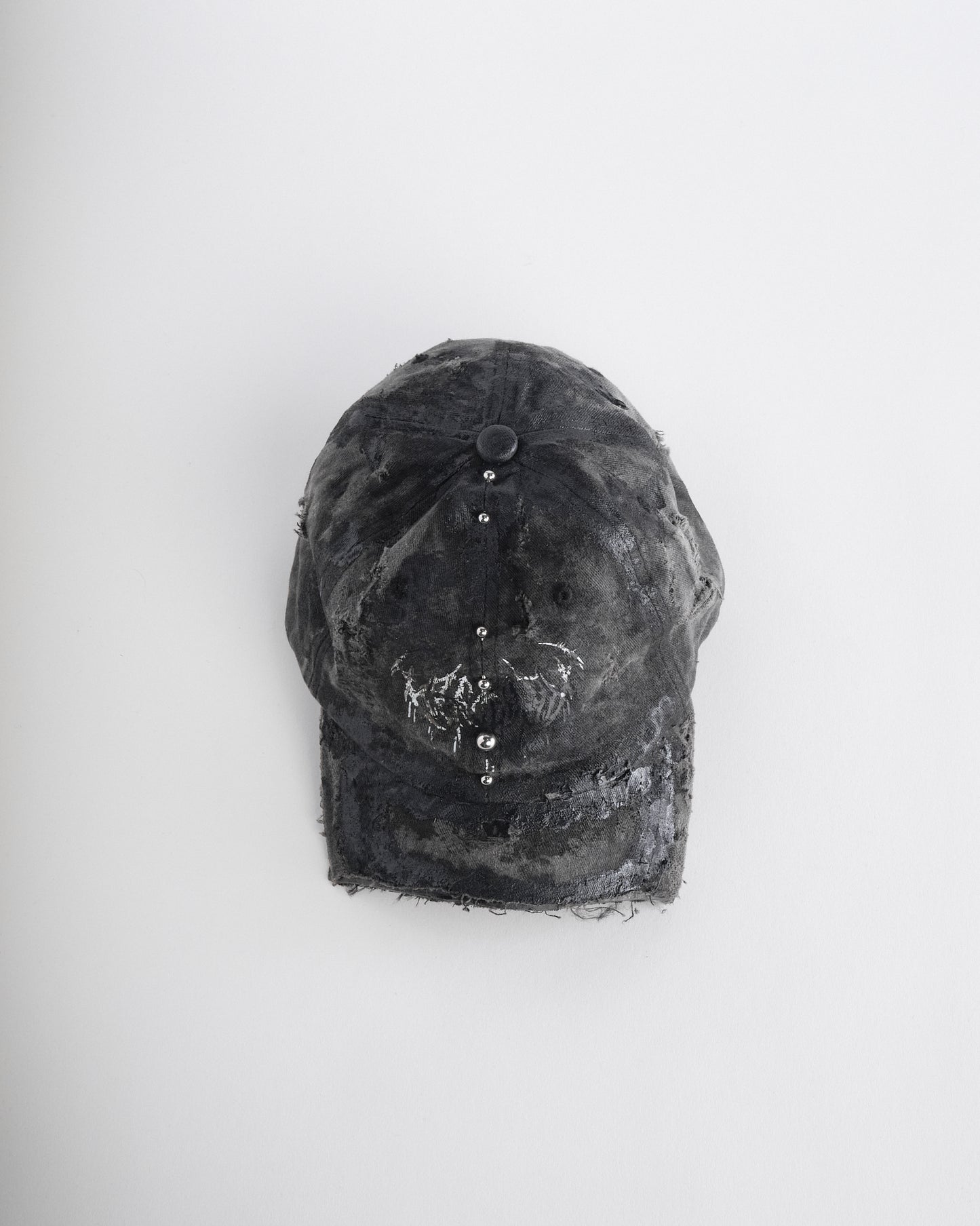 Front top of Black distressed half-visor hat with barbed-wire logo, adjustable strap, black paint details, and stainless steel piercings along the brim.