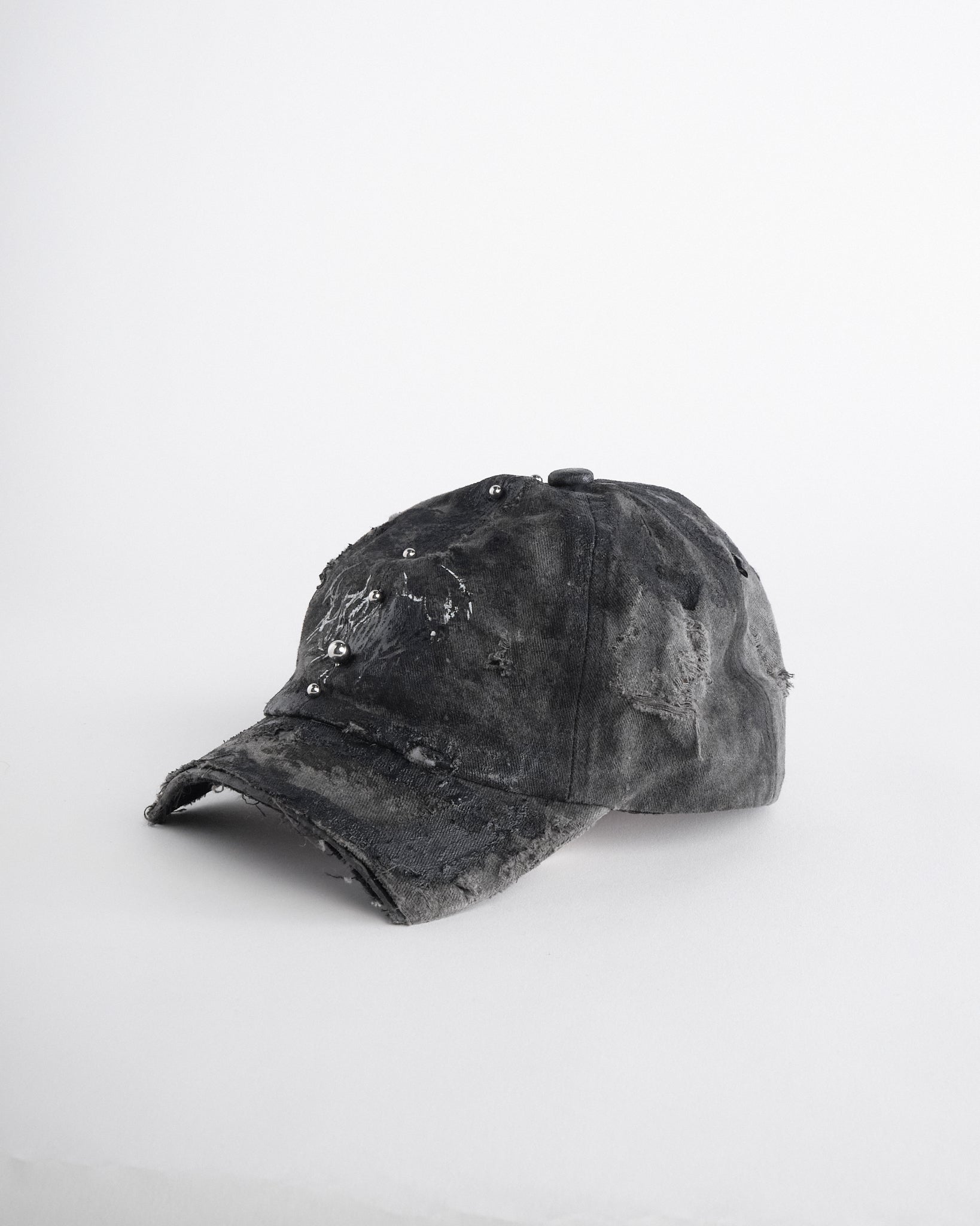 Left of Black distressed half-visor hat with barbed-wire logo, adjustable strap, black paint details, and stainless steel piercings along the brim.