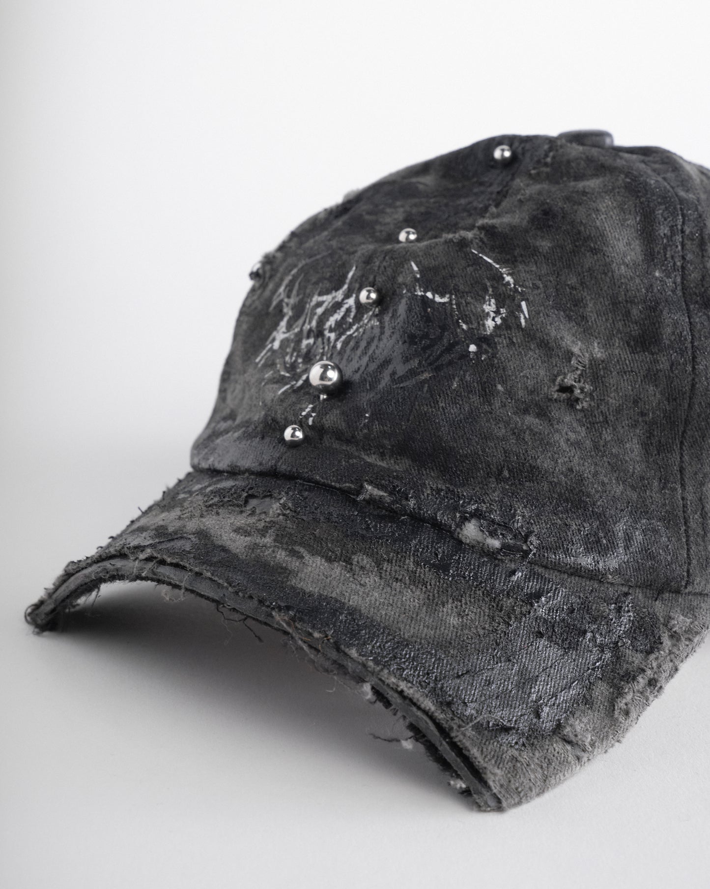 Front visor detail of Black distressed half-visor hat with barbed-wire logo, adjustable strap, black paint details, and stainless steel piercings along the brim.