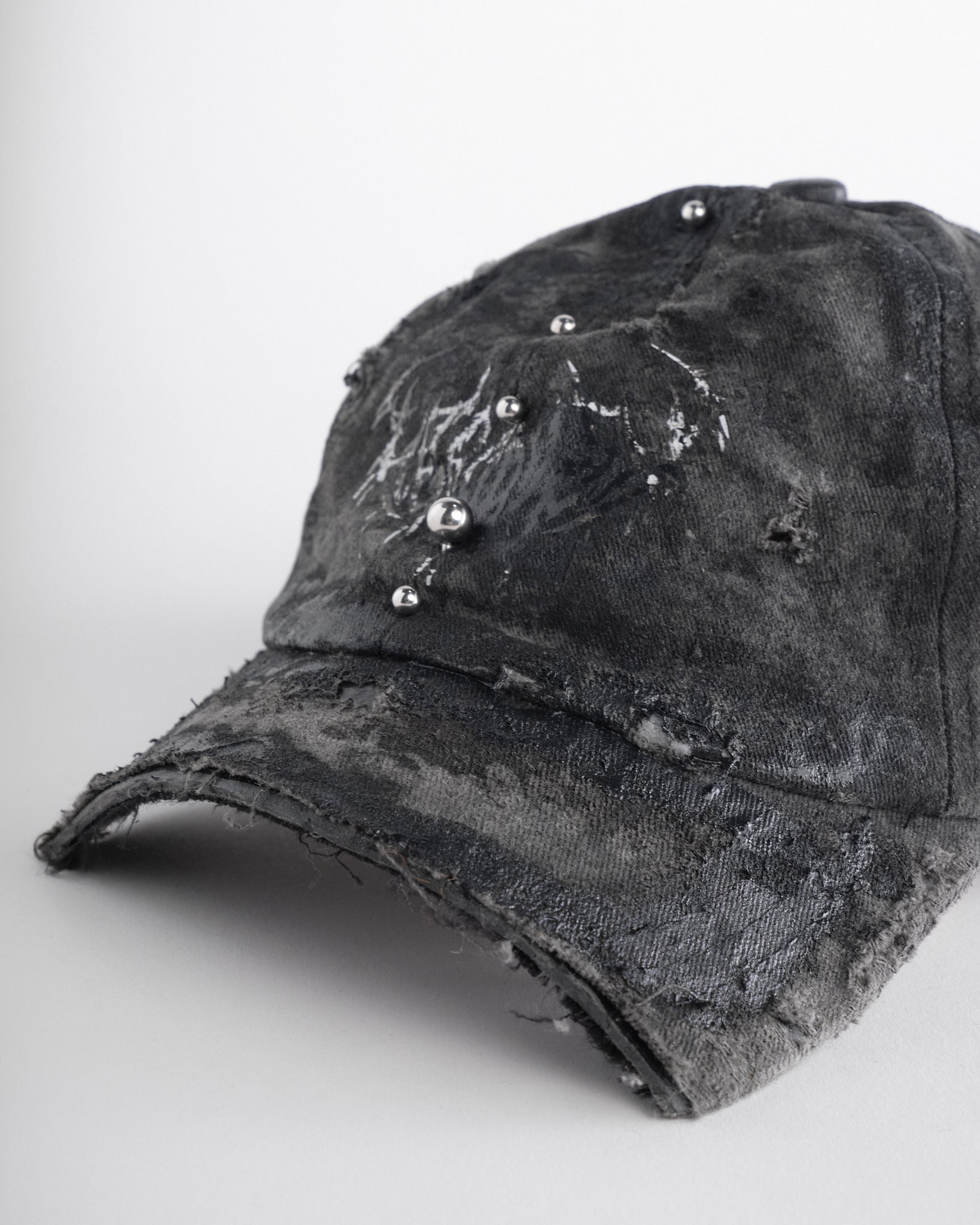 Front visor detail of Black distressed half-visor hat with barbed-wire logo, adjustable strap, black paint details, and stainless steel piercings along the brim.