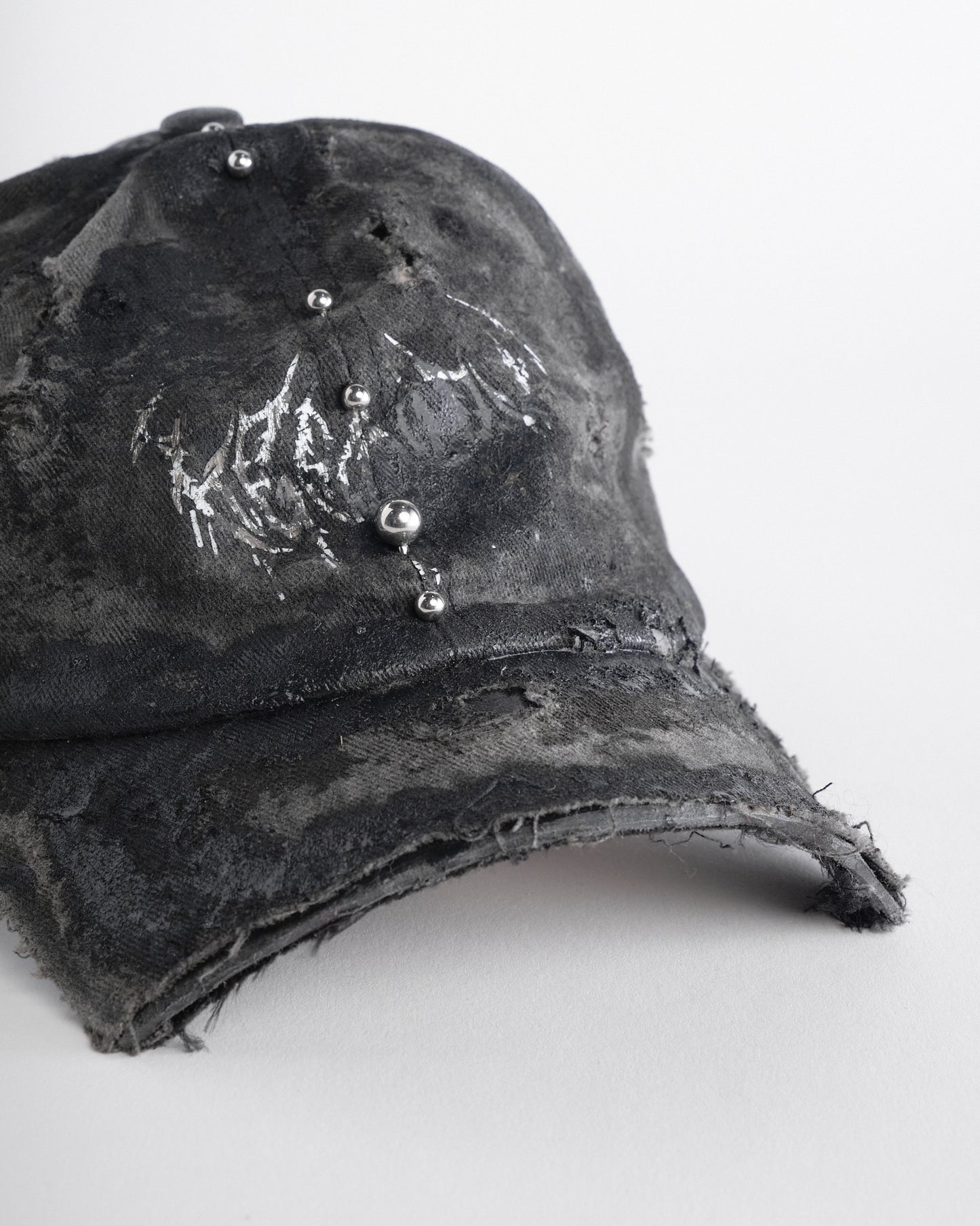 Front right of Black distressed half-visor hat with barbed-wire logo, adjustable strap, black paint details, and stainless steel piercings along the brim.