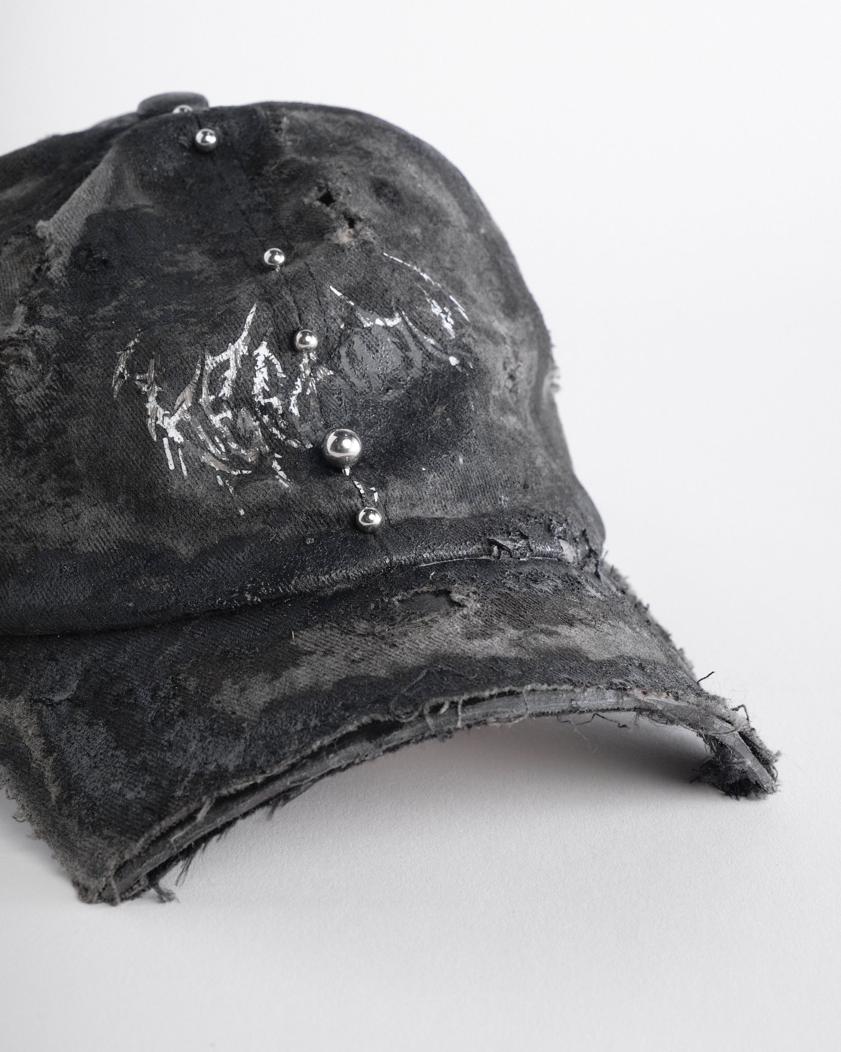 Front right of Black distressed half-visor hat with barbed-wire logo, adjustable strap, black paint details, and stainless steel piercings along the brim.