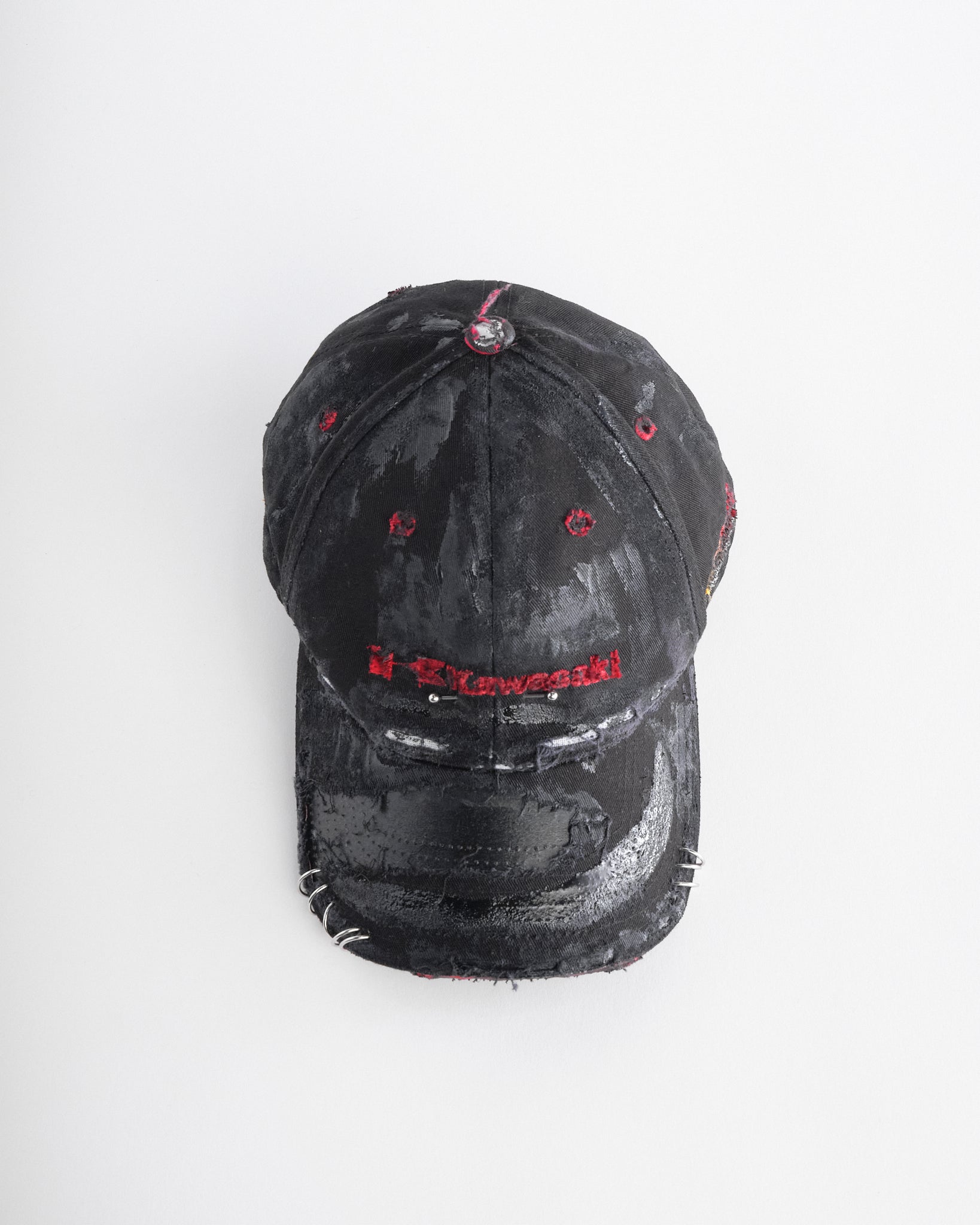 Top of ASTROBOI* x Kawasaki black distressed hat with pierced logo, deconstructed visor, stainless steel piercings, adjustable strap, handmade in NYC.