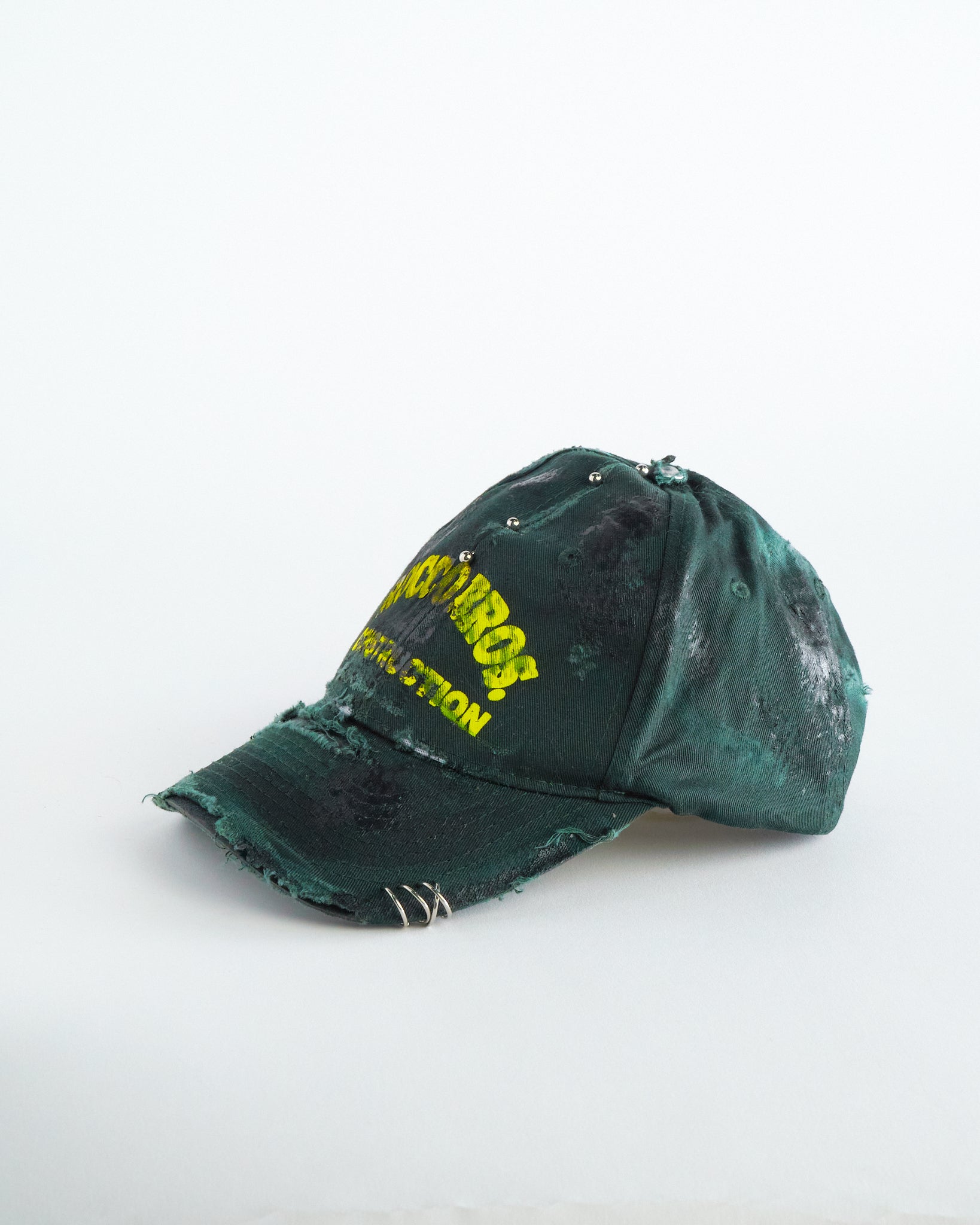 Left of ASTROBOI* Rocco Bros green construction hat with black grease distressing, stainless steel piercings, adjustable strap, handmade in NYC.