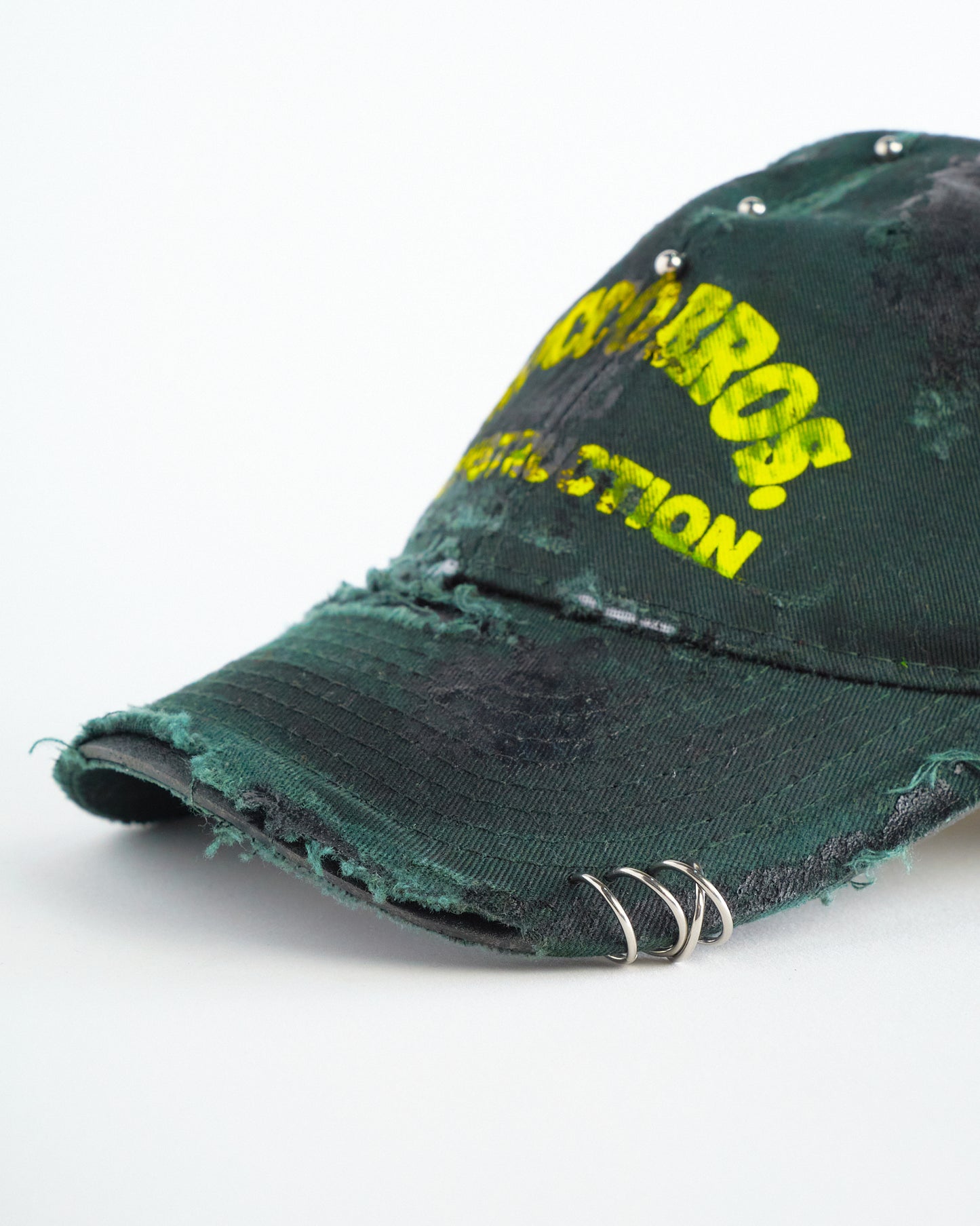Front visor detail of ASTROBOI* Rocco Bros green construction hat with black grease distressing, stainless steel piercings, adjustable strap, handmade in NYC.