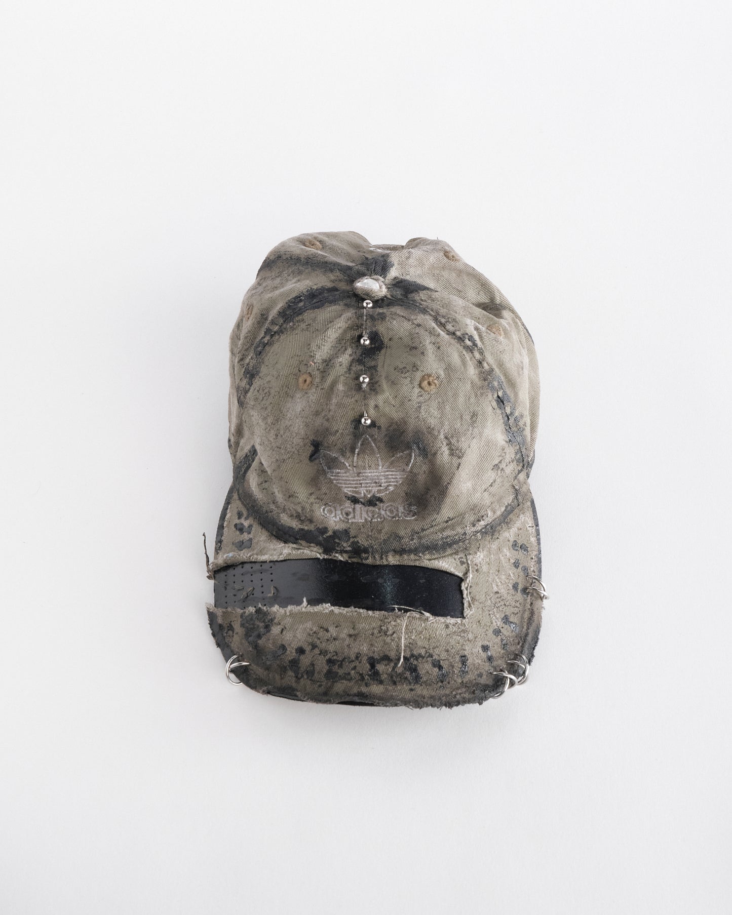 overview of ASTROBOI* x Adidas tan distressed hat with black paint detailing, Adidas logo at front, and stainless steel piercings, customized in NYC.
