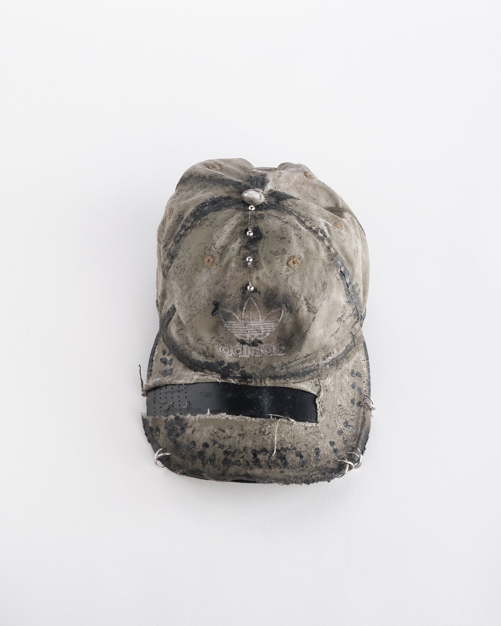 overview of ASTROBOI* x Adidas tan distressed hat with black paint detailing, Adidas logo at front, and stainless steel piercings, customized in NYC.
