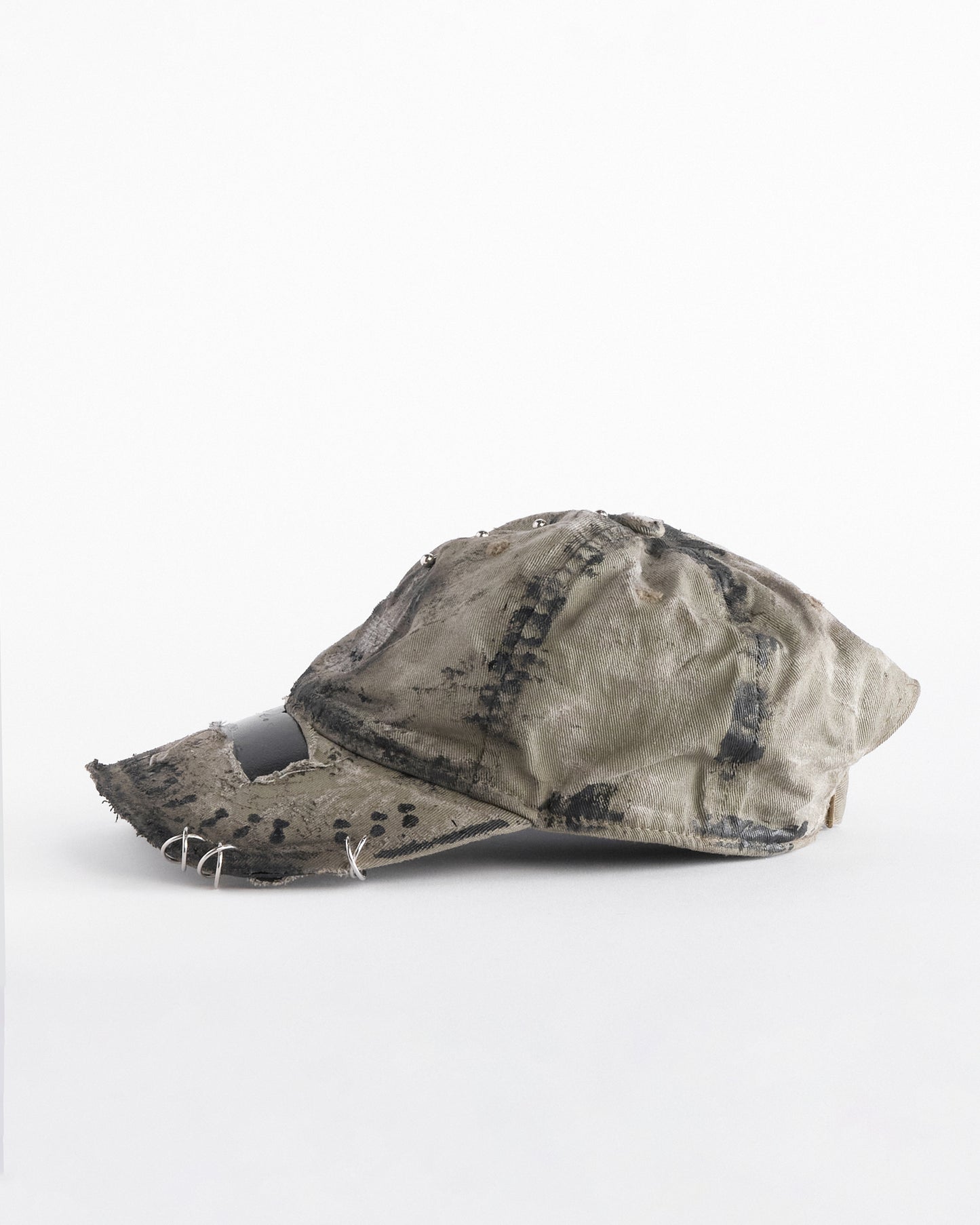 Left of ASTROBOI* x Adidas tan distressed hat with black paint detailing, Adidas logo at front, and stainless steel piercings, customized in NYC.