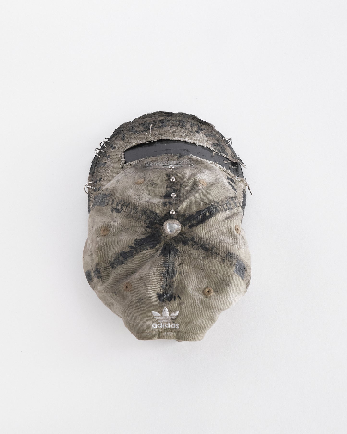 Top of ASTROBOI* x Adidas tan distressed hat with black paint detailing, Adidas logo at front, and stainless steel piercings, customized in NYC.