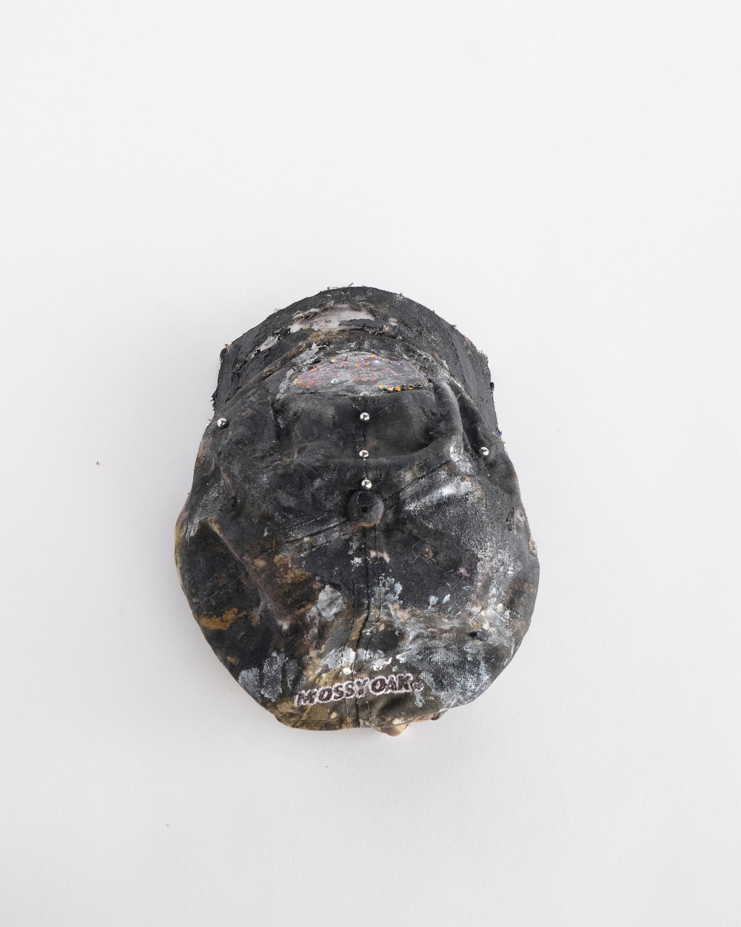 Back above side of ASTROBOI* x Mossy Oak brown real tree camo half visor hat with rhinestone resin logo and stainless steel piercings.