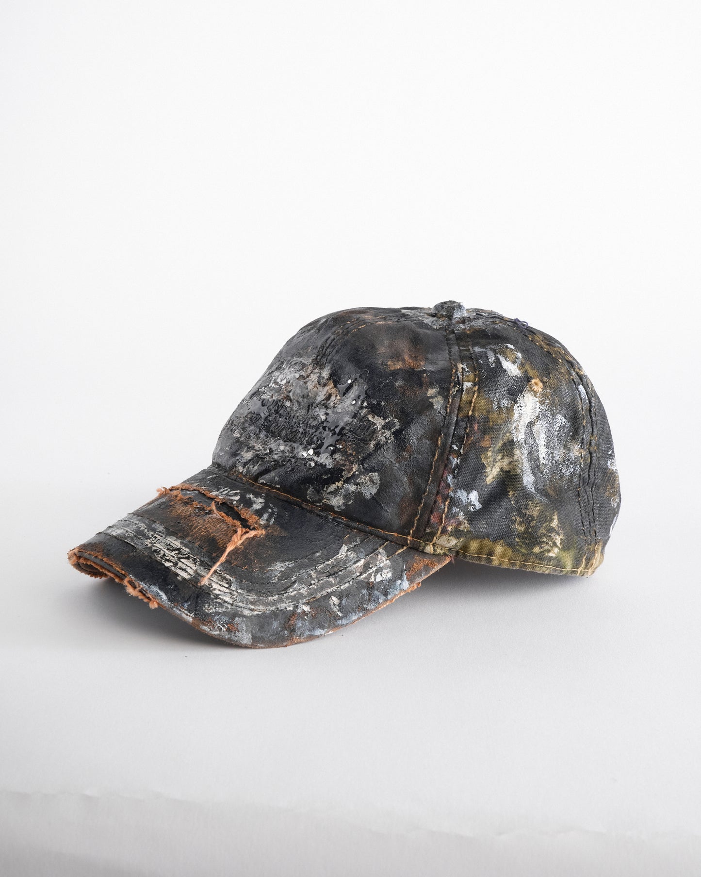 Left of ASTROBOI* x Mossy Oak brown RealTree camo hat with rhinestones, distressed paint details, and leather visor, adjustable fit.