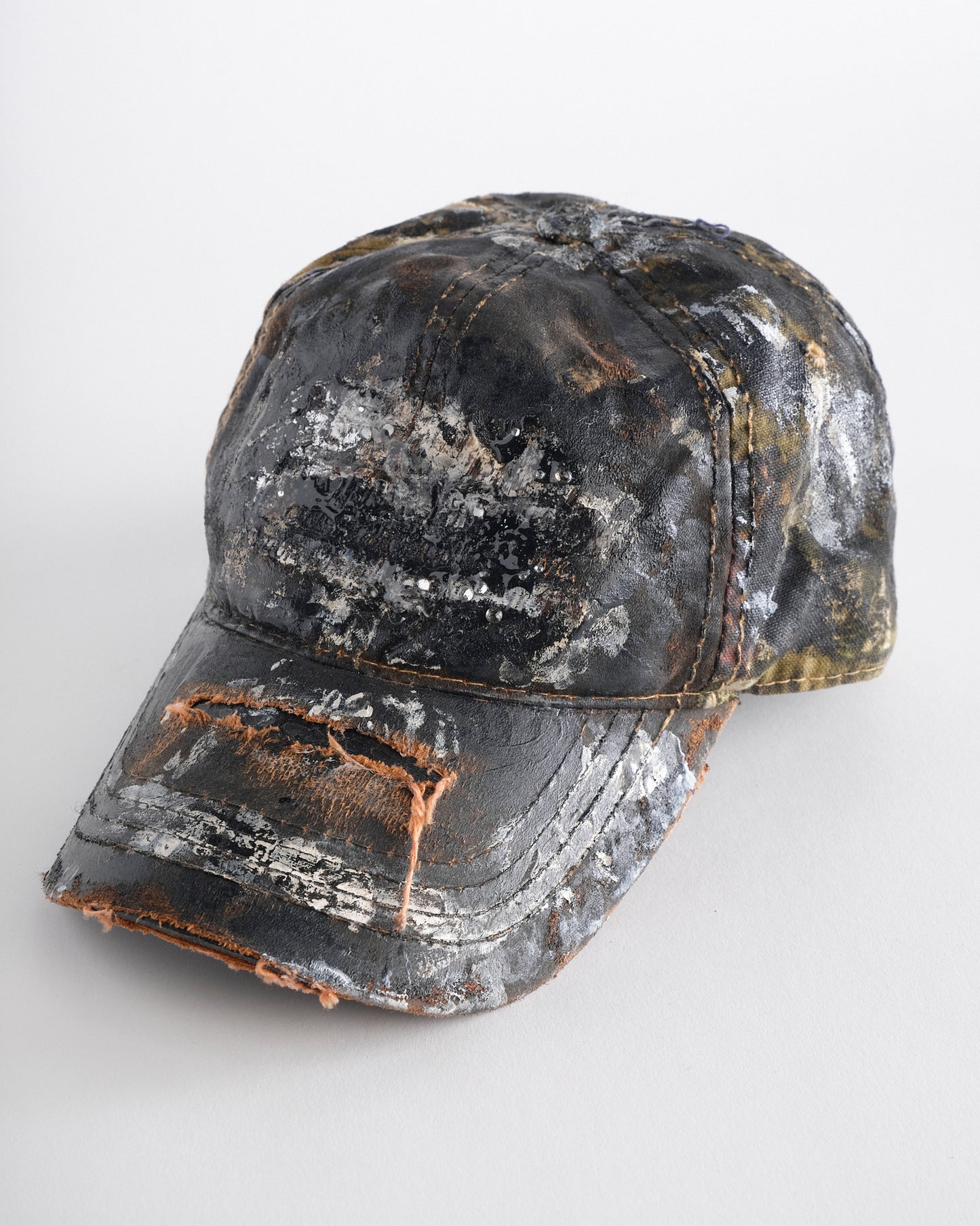 Logo detail on ASTROBOI* x Mossy Oak brown RealTree camo hat with rhinestones, distressed paint details, and leather visor, adjustable fit.