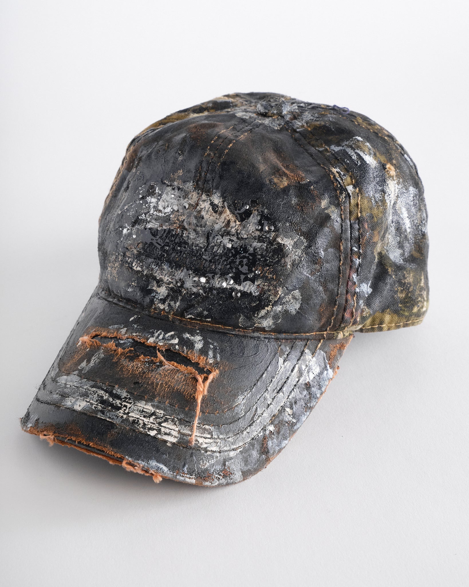 Logo detail on ASTROBOI* x Mossy Oak brown RealTree camo hat with rhinestones, distressed paint details, and leather visor, adjustable fit.