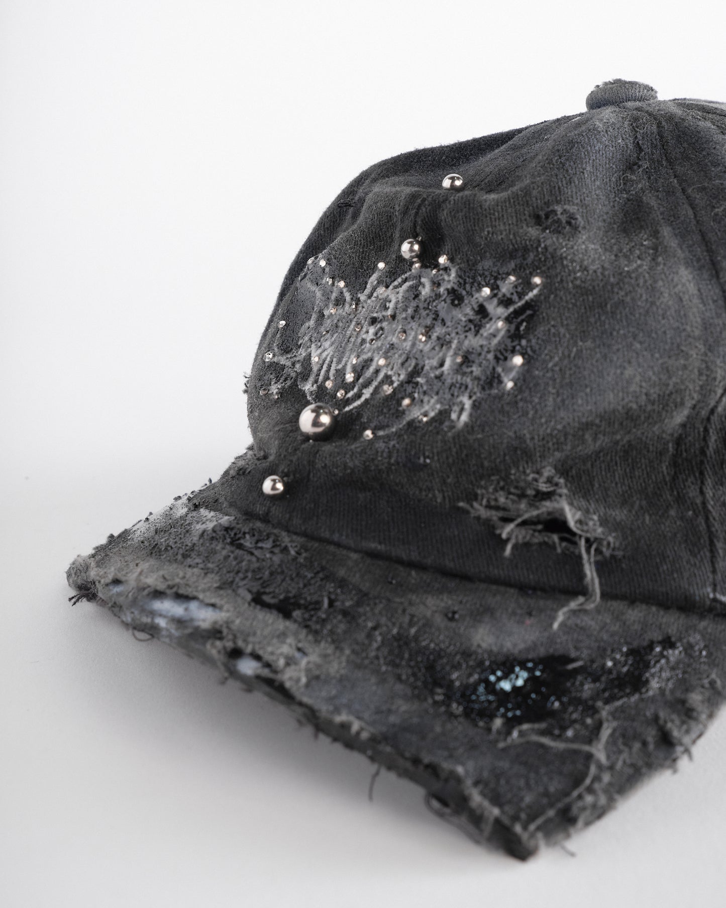 Logo detail of ASTROBOI* Chalk black distressed half-visor hat with white airbrush detailing, rhinestones, resin accents, and stainless steel piercings.