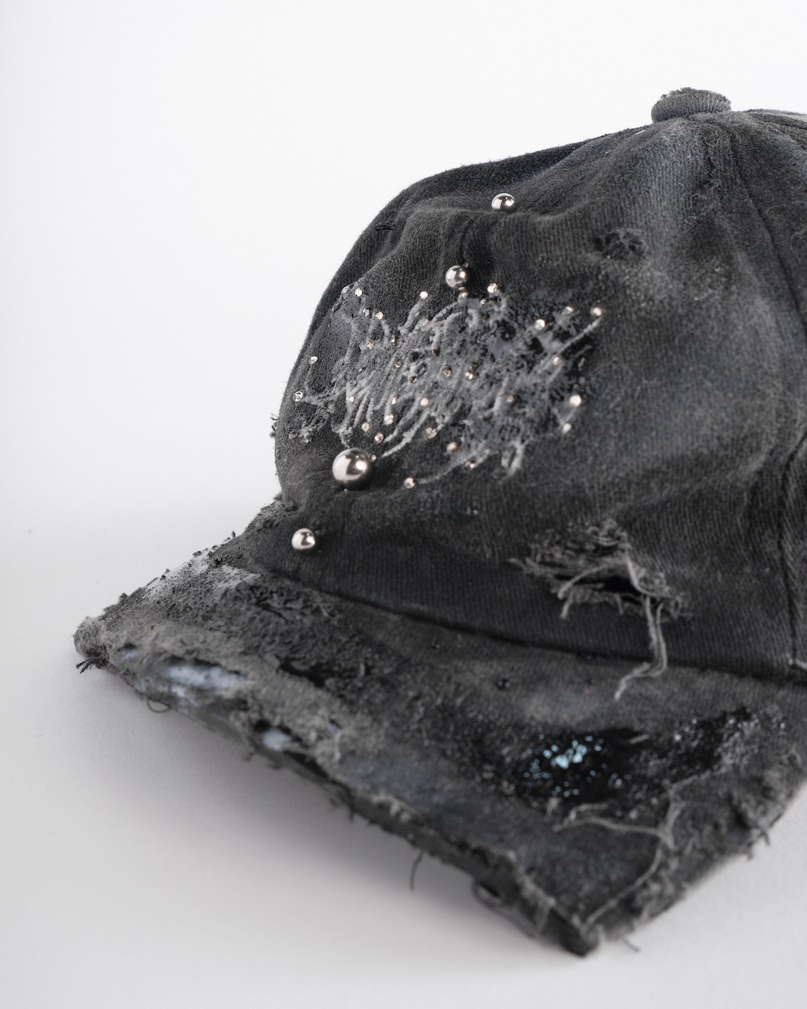 Logo detail of ASTROBOI* Chalk black distressed half-visor hat with white airbrush detailing, rhinestones, resin accents, and stainless steel piercings.