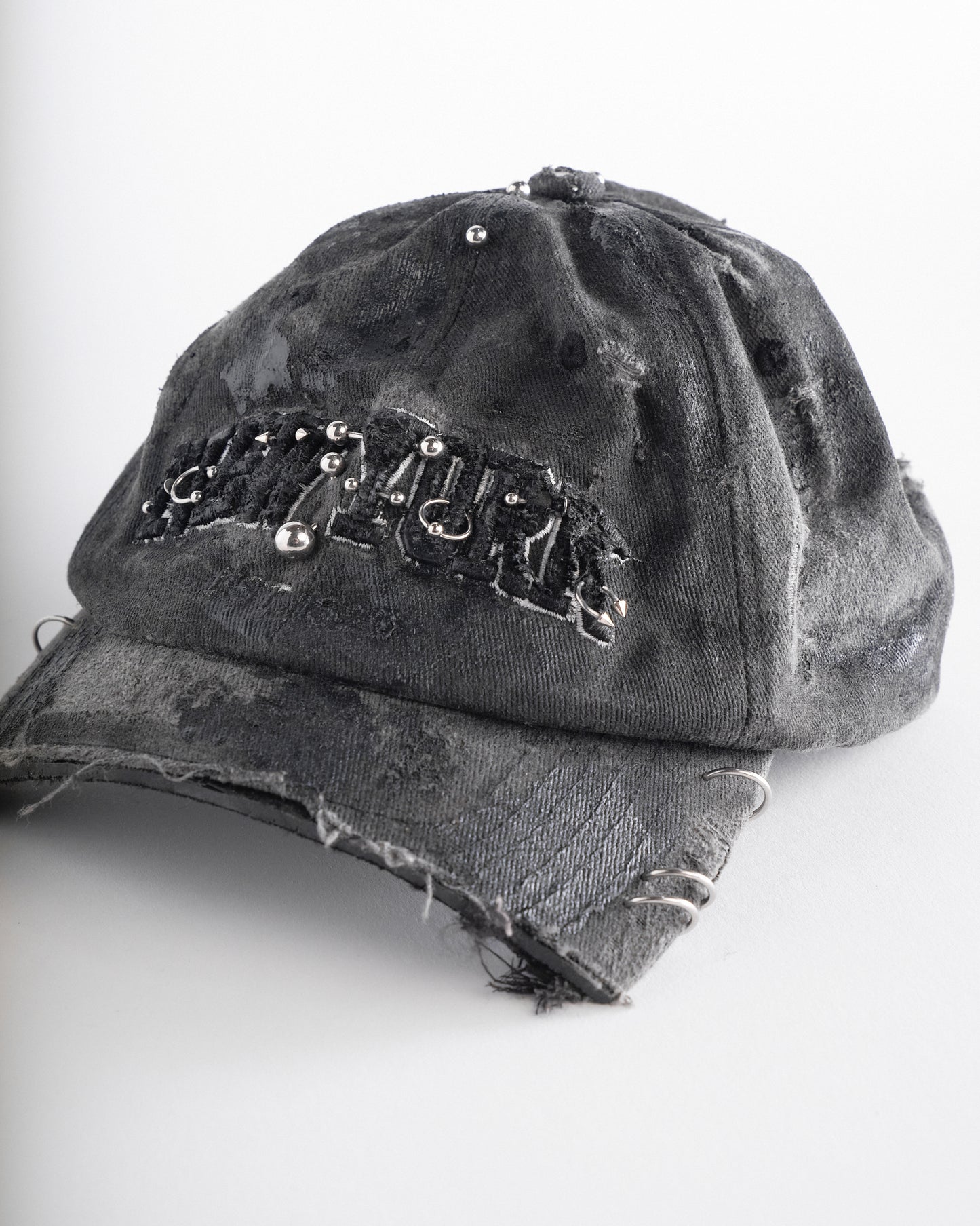 Left front detail of Black half-visor “New York” hat with embroidered front logo, stainless steel piercings, and an adjustable strap.