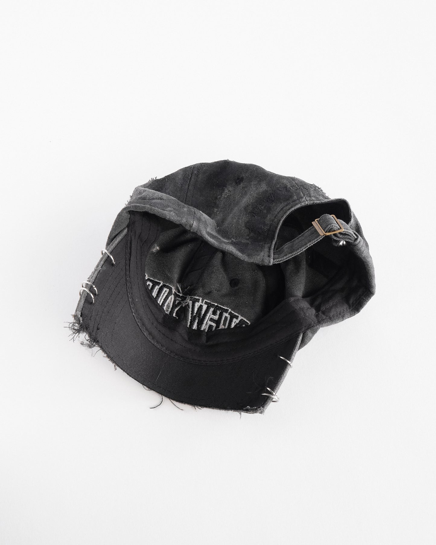 Interior side of Black half-visor “New York” hat with embroidered front logo, stainless steel piercings, and an adjustable strap.