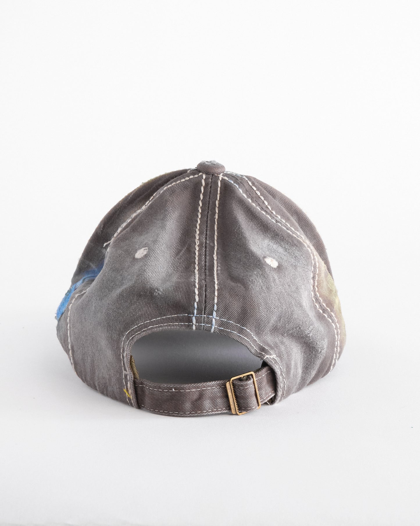 Back of Brown-green ASTROBOI* hat featuring a metallic Hawaii logo with multicolored rhinestones, distressed visor, and resin-coated safety pin detail.