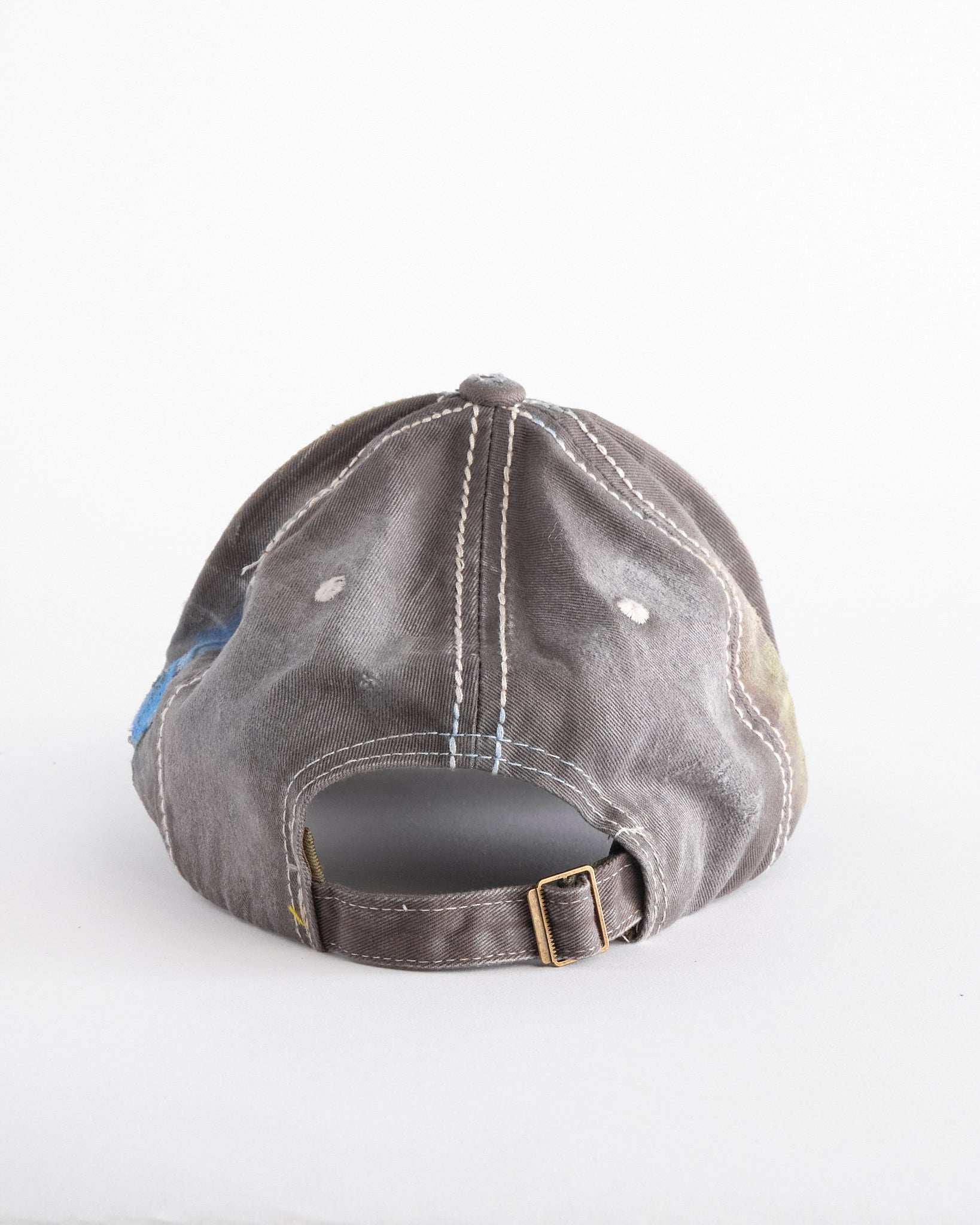 Back of Brown-green ASTROBOI* hat featuring a metallic Hawaii logo with multicolored rhinestones, distressed visor, and resin-coated safety pin detail.