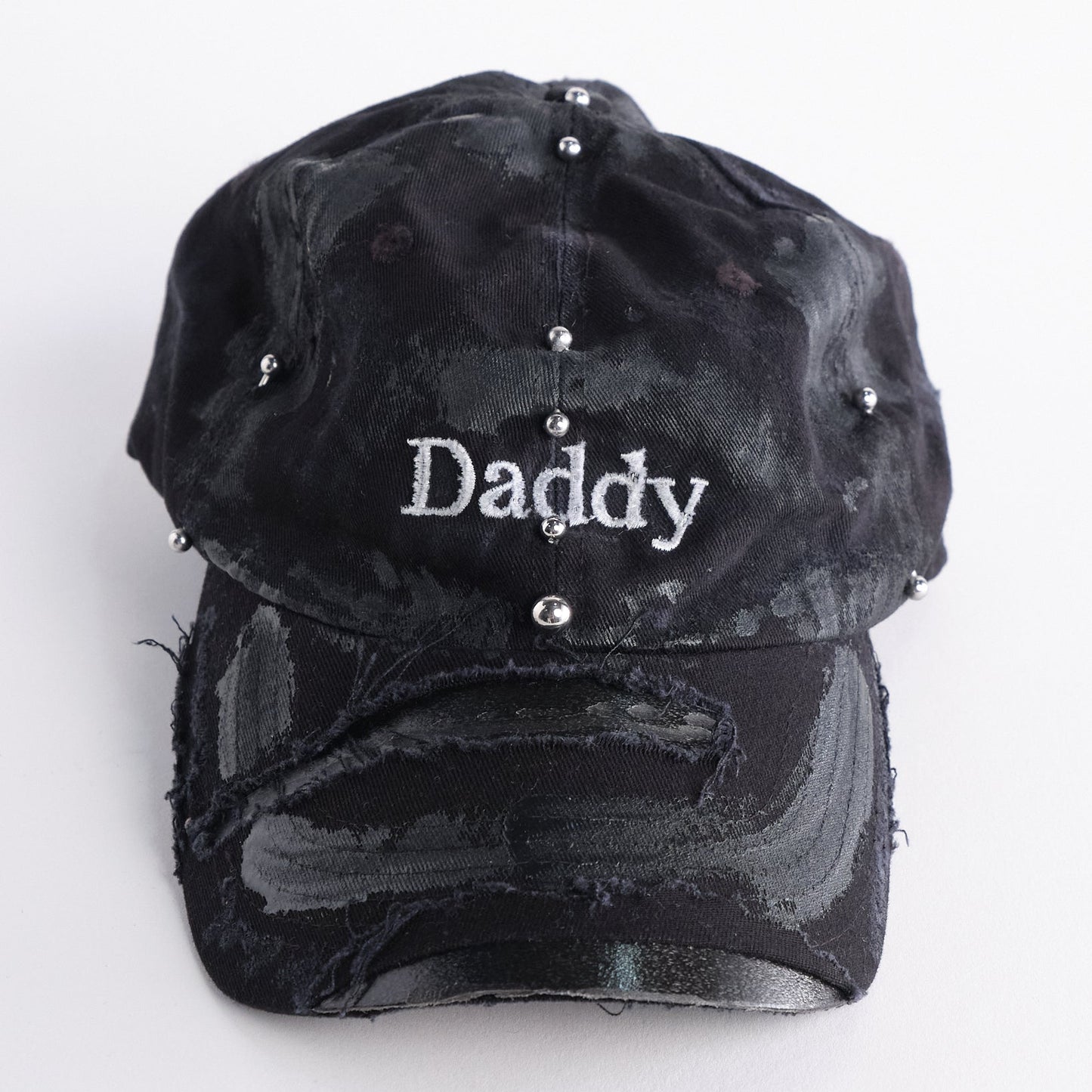 Front of side of Black distressed ASTROBOI* ‘Daddy’ hat with custom paint detailing and stainless steel piercings, handcrafted in NYC.