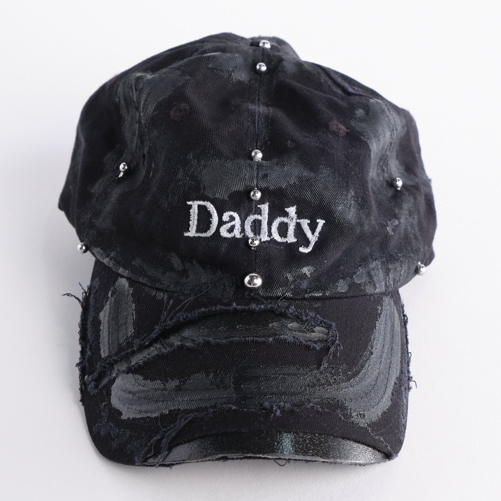Front of side of Black distressed ASTROBOI* ‘Daddy’ hat with custom paint detailing and stainless steel piercings, handcrafted in NYC.
