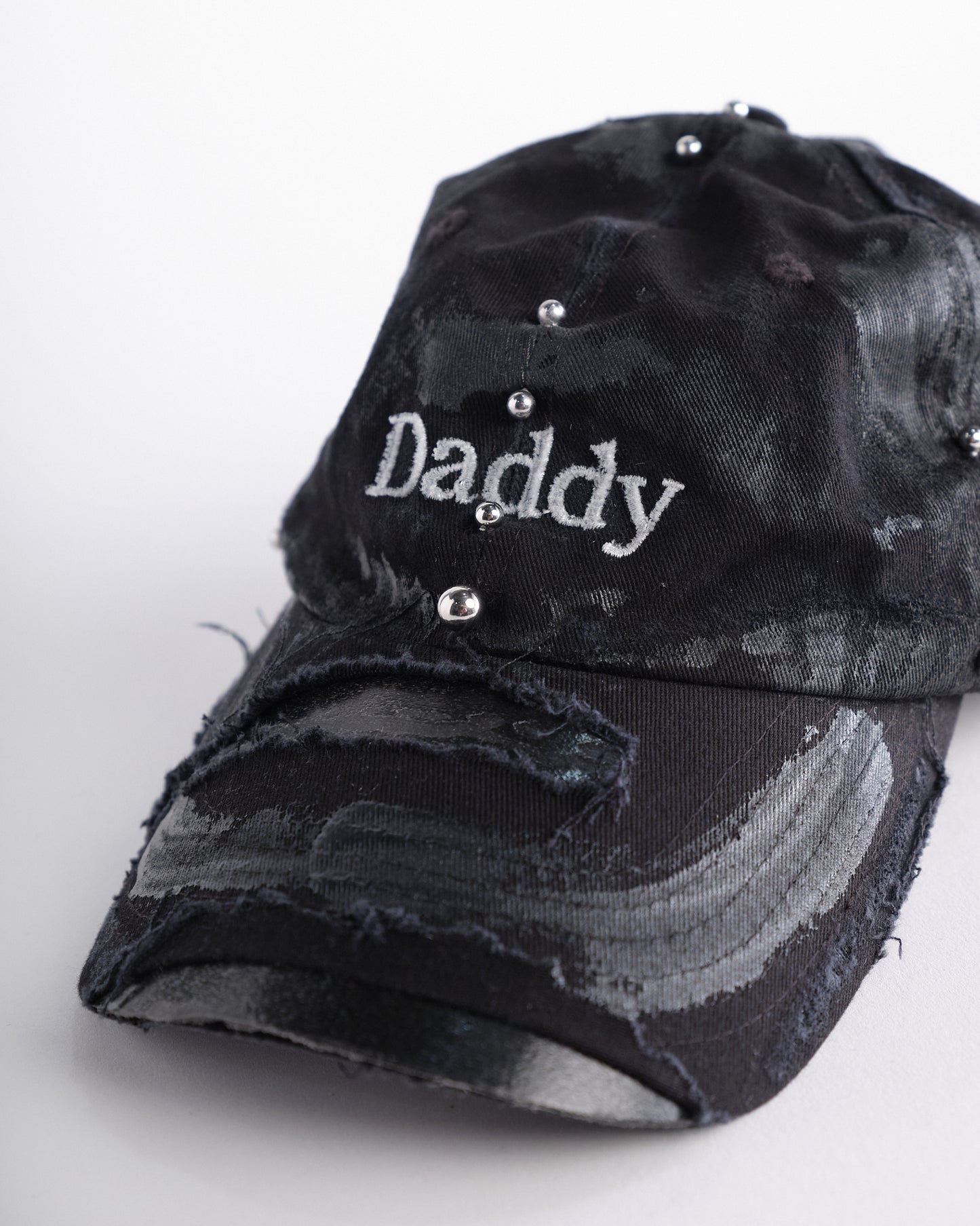 Close up detail of Black distressed ASTROBOI* ‘Daddy’ hat with custom paint detailing and stainless steel piercings, handcrafted in NYC.
