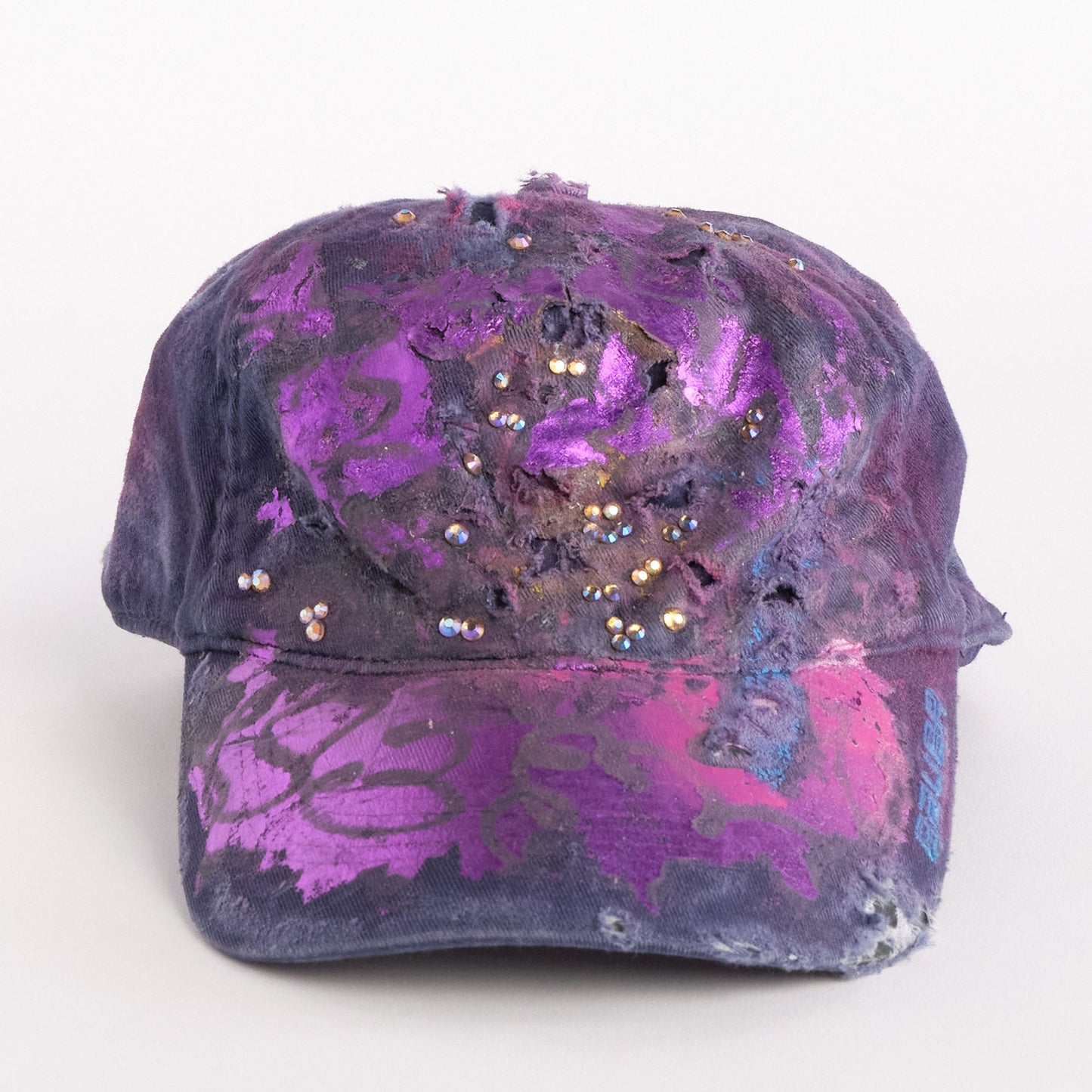 Front of ASTROBOI* x Bauer purple distressed hat with metallic paint detailing, clustered rhinestones, and closed-back fit, handmade and customized in NYC.