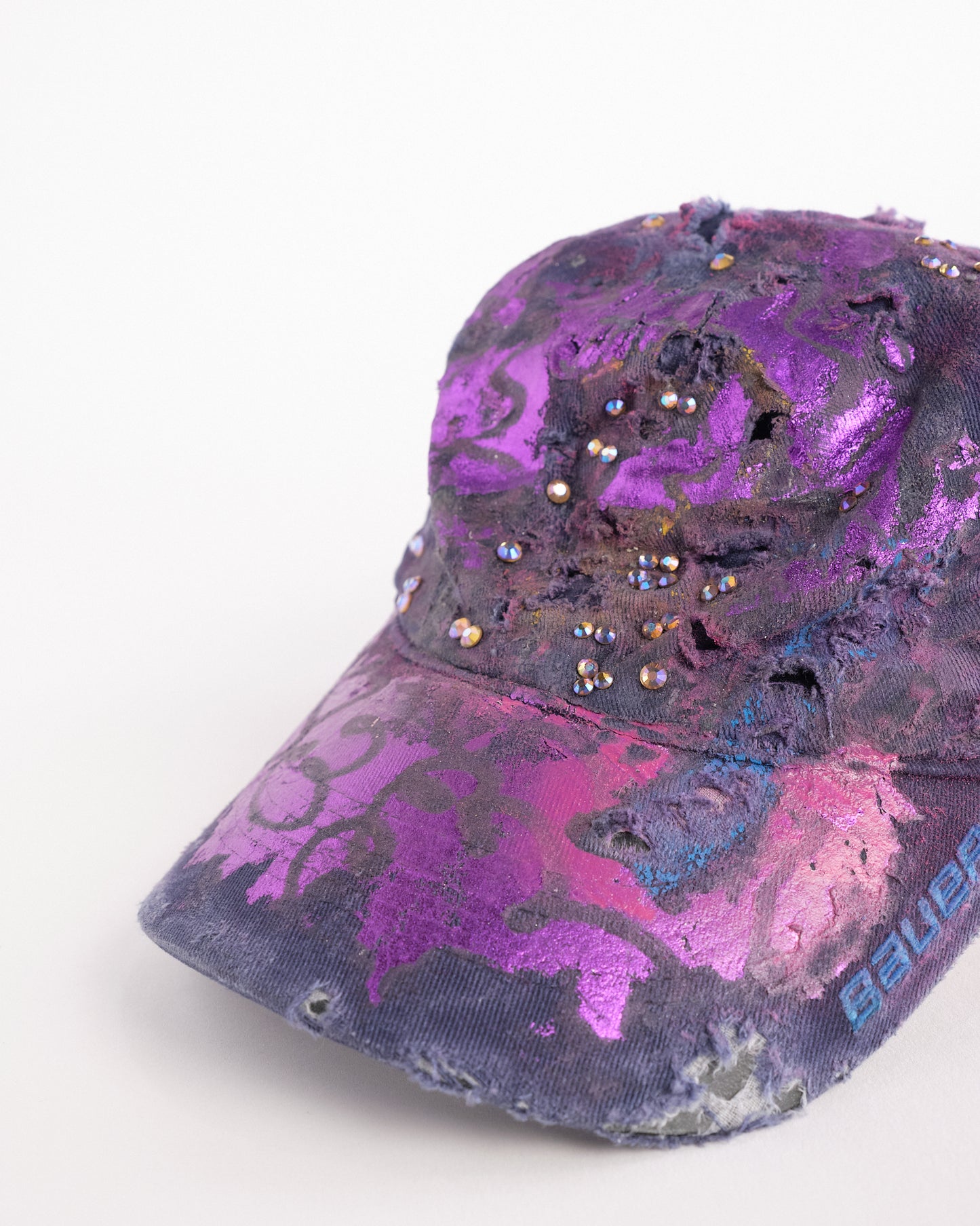 Left detail of ASTROBOI* x Bauer purple distressed hat with metallic paint detailing, clustered rhinestones, and closed-back fit, handmade and customized in NYC.