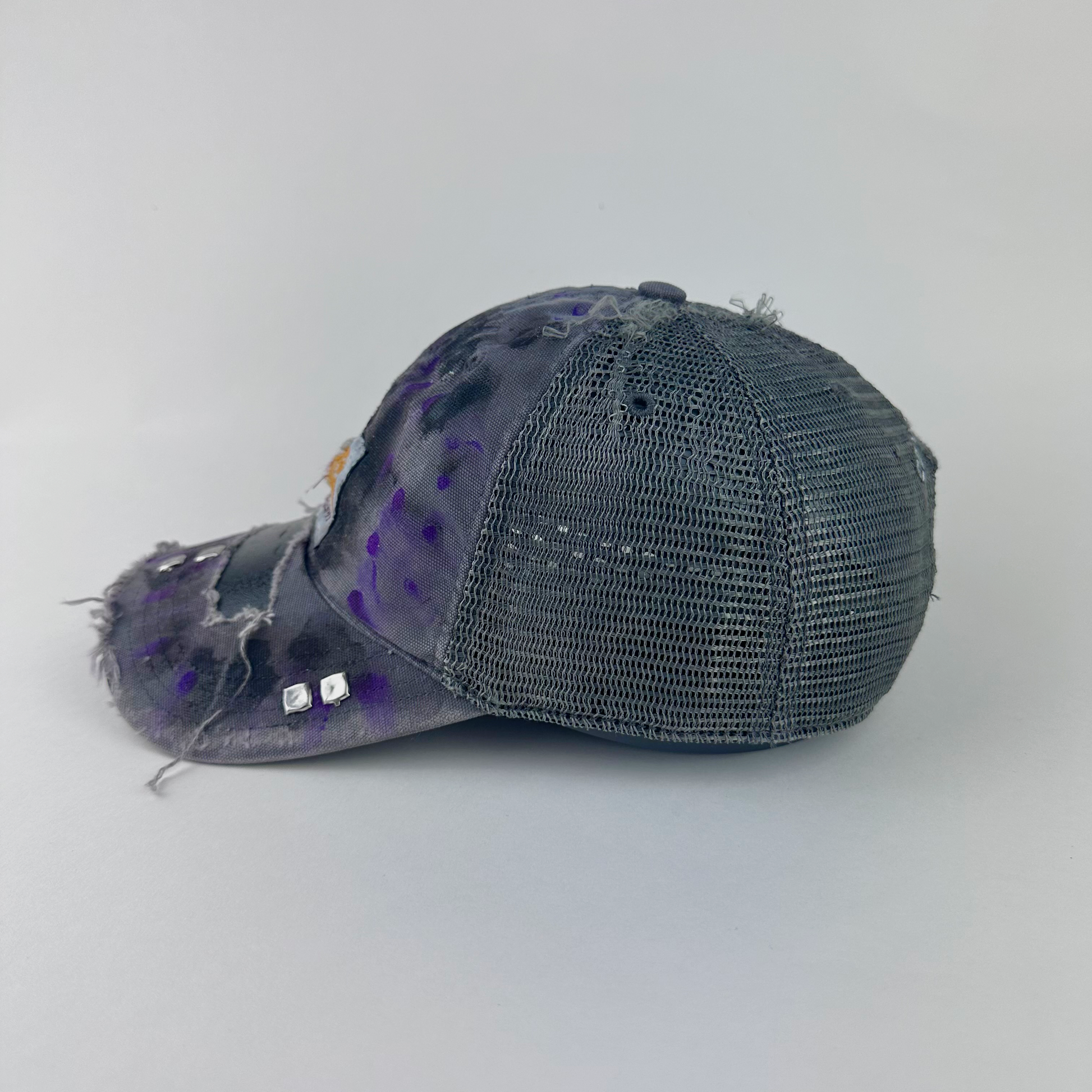 Left side detail of ASTROBOI* x Carhartt 'Amethyst' showing deconstructed visor, silver studs, and purple and black paint treatment on gray Carhartt hat.