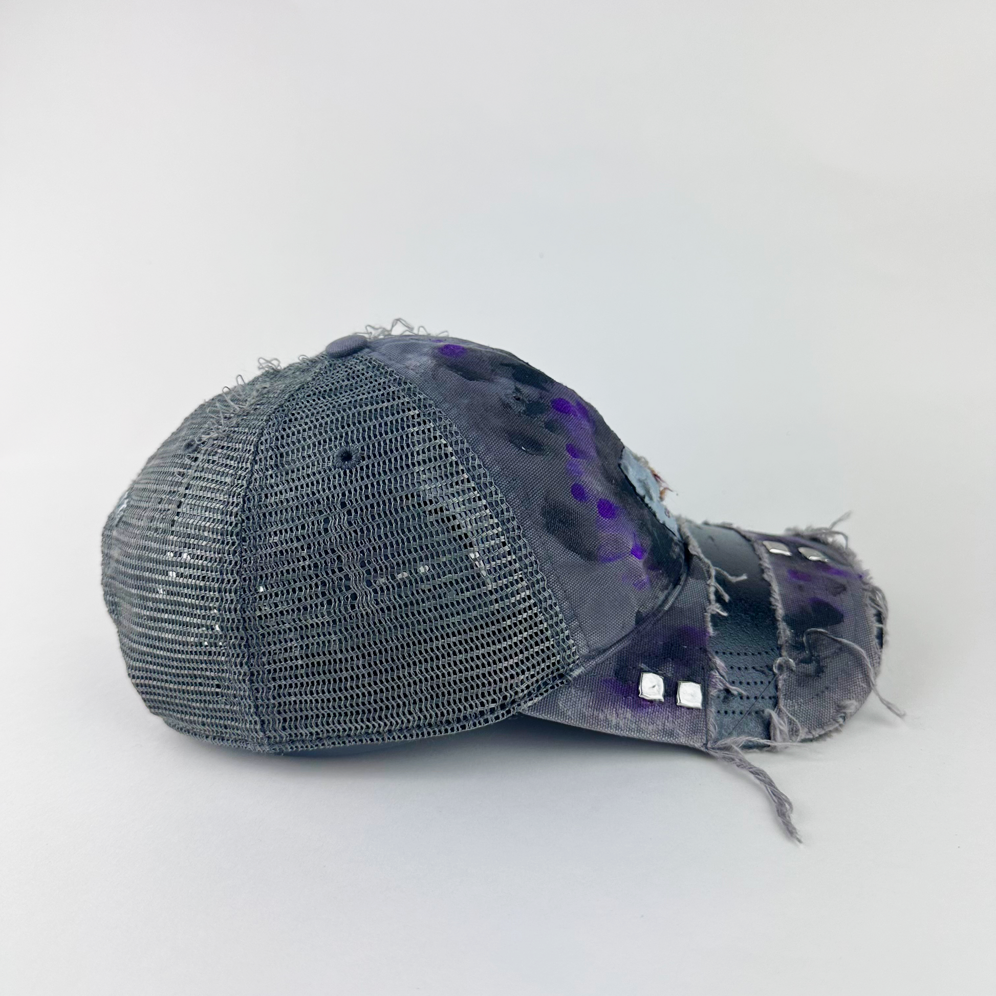 Right side detail of ASTROBOI* x Carhartt 'Amethyst' showing silver studded visor detail and black and purple paint treatment on gray distressed base.