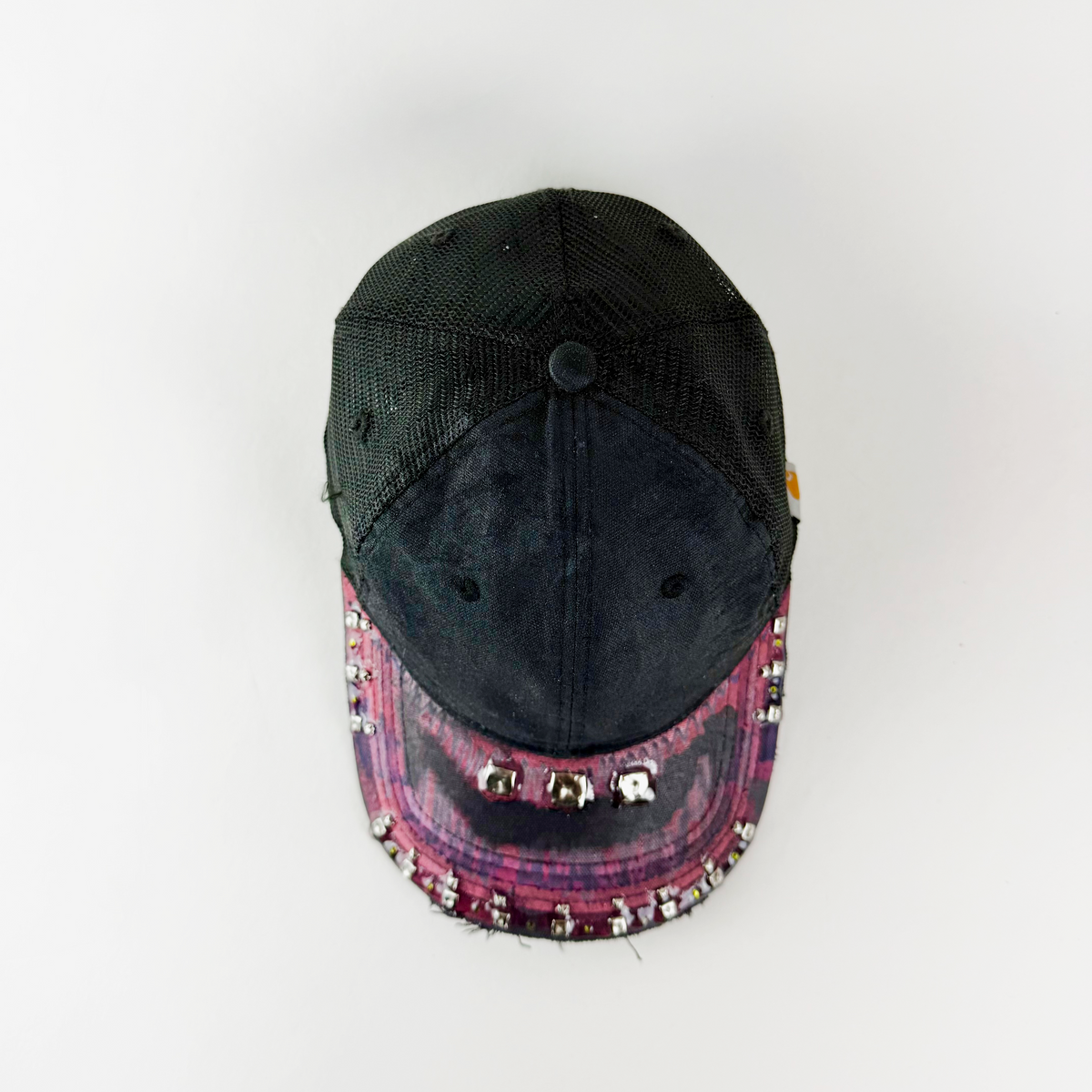 A distressed black trucker-style cap with a dark pink and purple plaid brim, embellished with rhinestones and silver studs, photographed from a top-down angle on a white background.