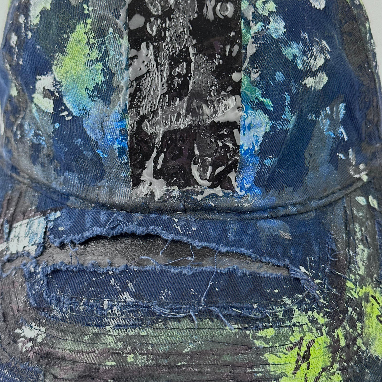 Close-up of ASTROBOI* 'Coral' showing black, white, and blue speckled paint splatter and melted duct tape detail sealed under 3D wet resin on deconstructed visor.