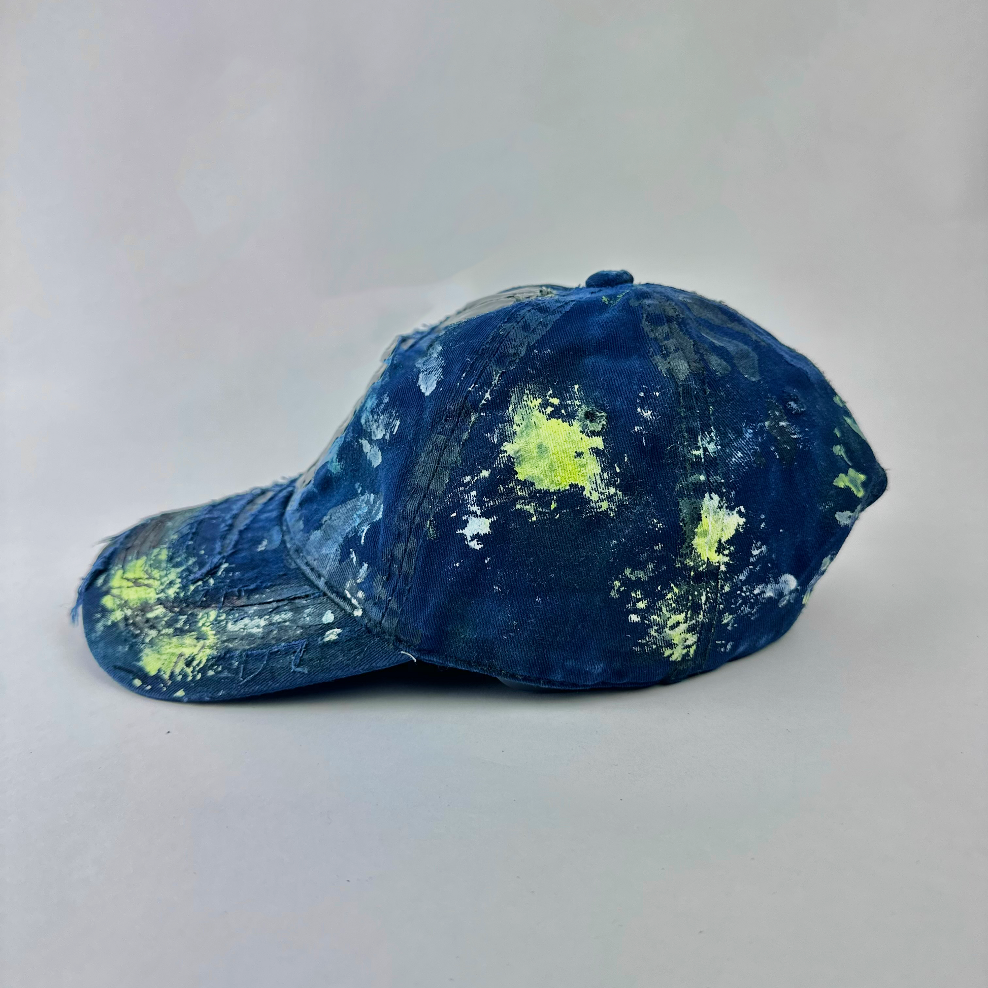 Left side detail of ASTROBOI* 'Coral' showing blue distressed fabric, speckled paint splatter, and deconstructed visor with resin detail.