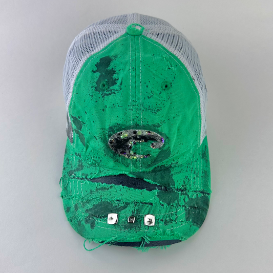 ASTROBOI* x Costa del Mar 'Jade' Y2K green rhinestone studded trucker hat with purple and green rhinestone-embellished Costa 'C' logo, silver studs on deconstructed visor, and black stained paint treatment, front view.
