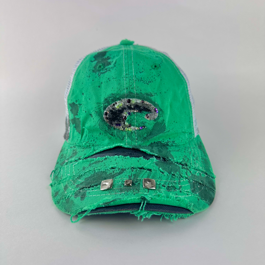 ASTROBOI* x Costa del Mar 'Jade' Y2K green rhinestone studded trucker hat with purple and green rhinestone-embellished Costa 'C' logo, silver studs on deconstructed visor, and black stained paint treatment, front view.