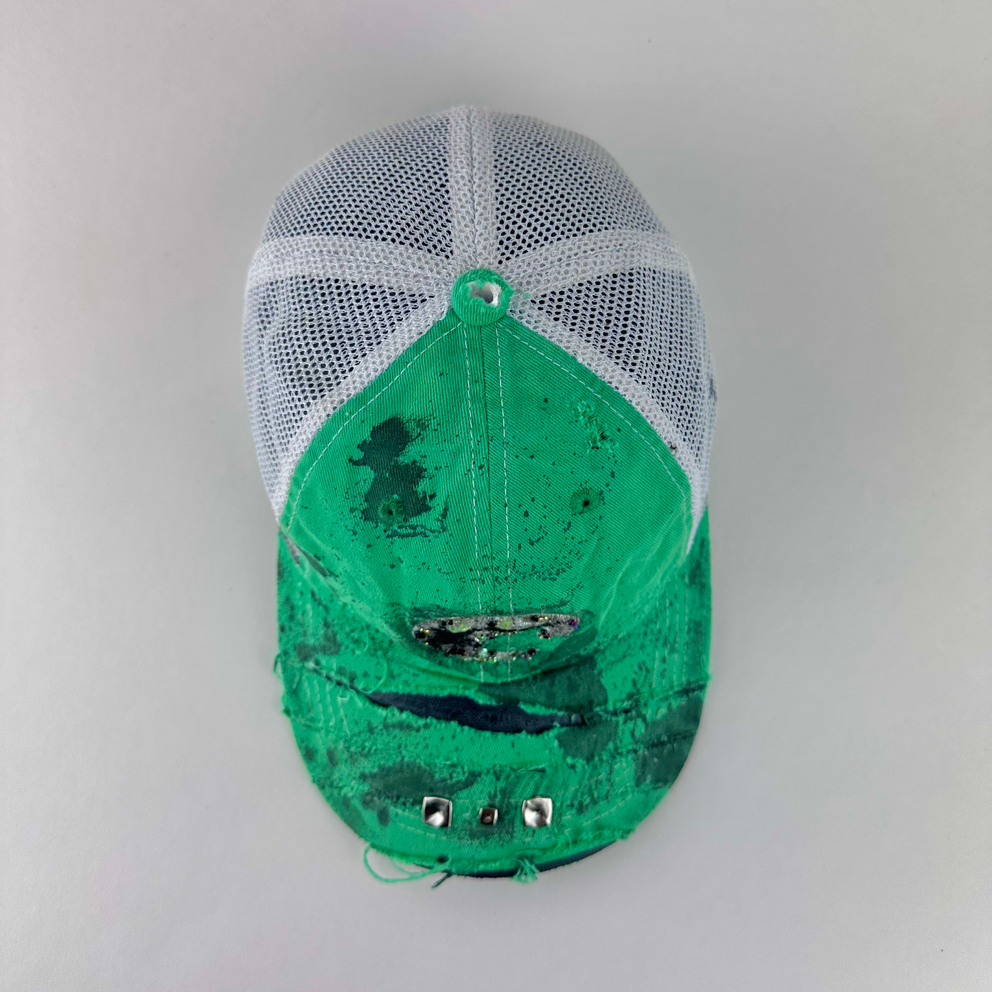 ASTROBOI* x Costa del Mar 'Jade' Y2K green rhinestone studded trucker hat with purple and green rhinestone-embellished Costa 'C' logo, silver studs on deconstructed visor, and black stained paint treatment, top view.