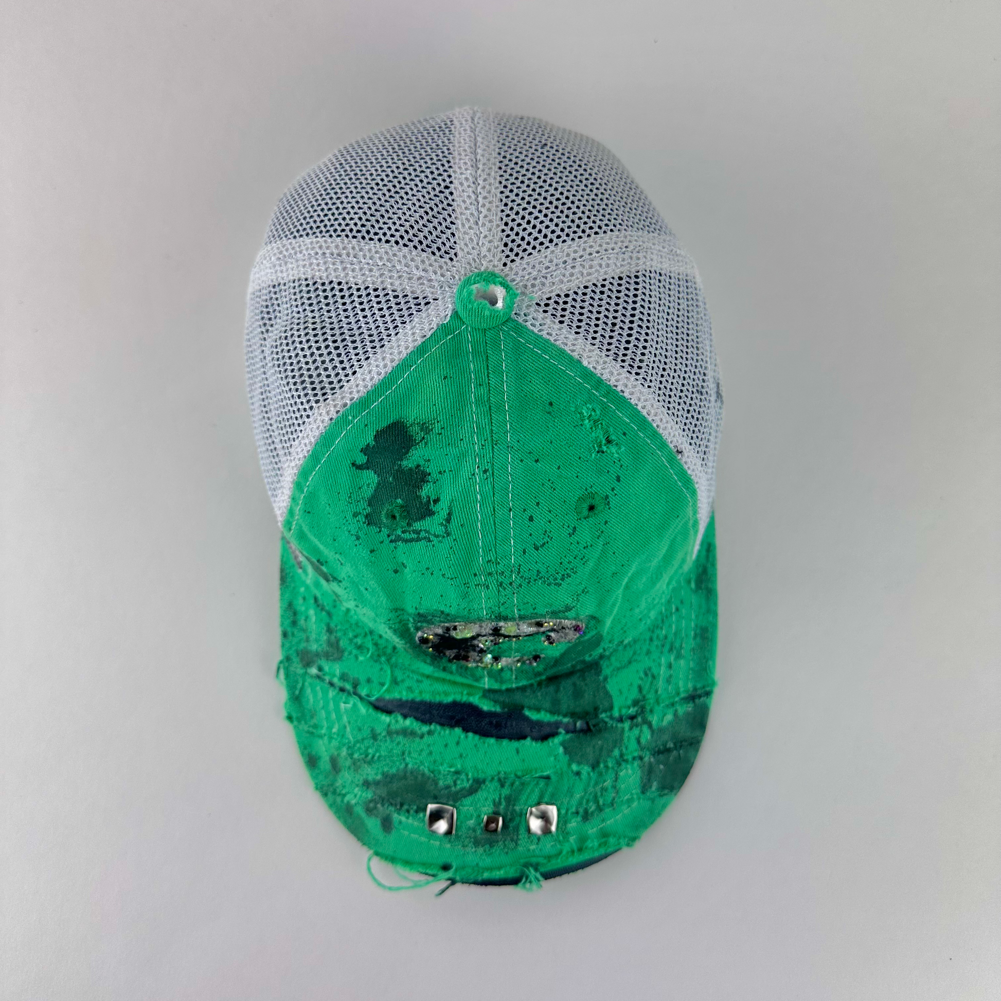 ASTROBOI* x Costa del Mar 'Jade' Y2K green rhinestone studded trucker hat with purple and green rhinestone-embellished Costa 'C' logo, silver studs on deconstructed visor, and black stained paint treatment, top view.