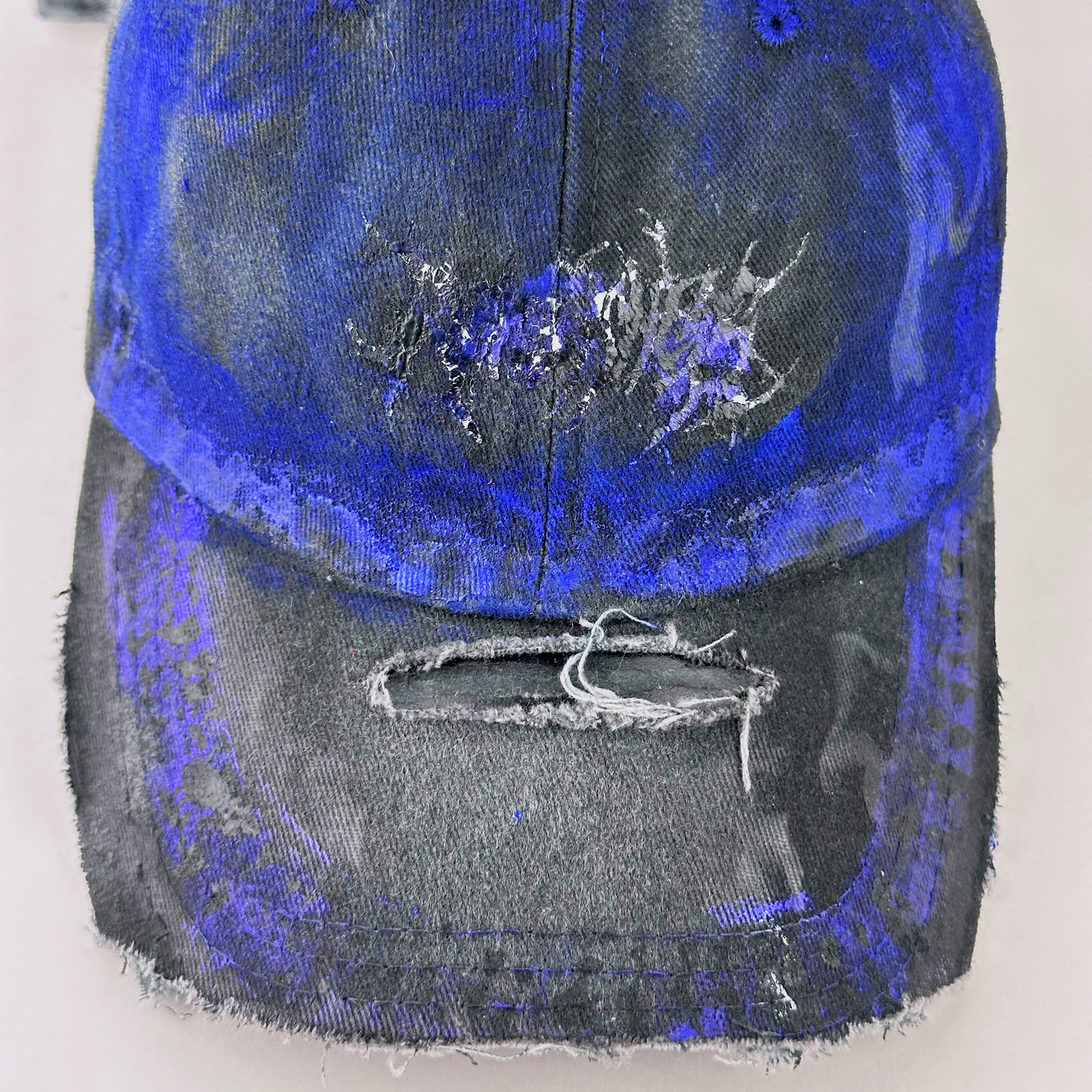 Close-up of ASTROBOI* 'Damian' showing indie barbed wire design detail and custom blue haze paint treatment on gray and black distressed fabric.