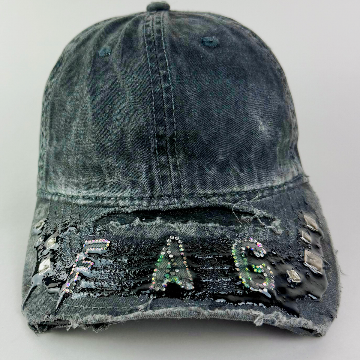 Close-up of multicolor rhinestone “FAG” lettering in silver, pink, and green on black denim.