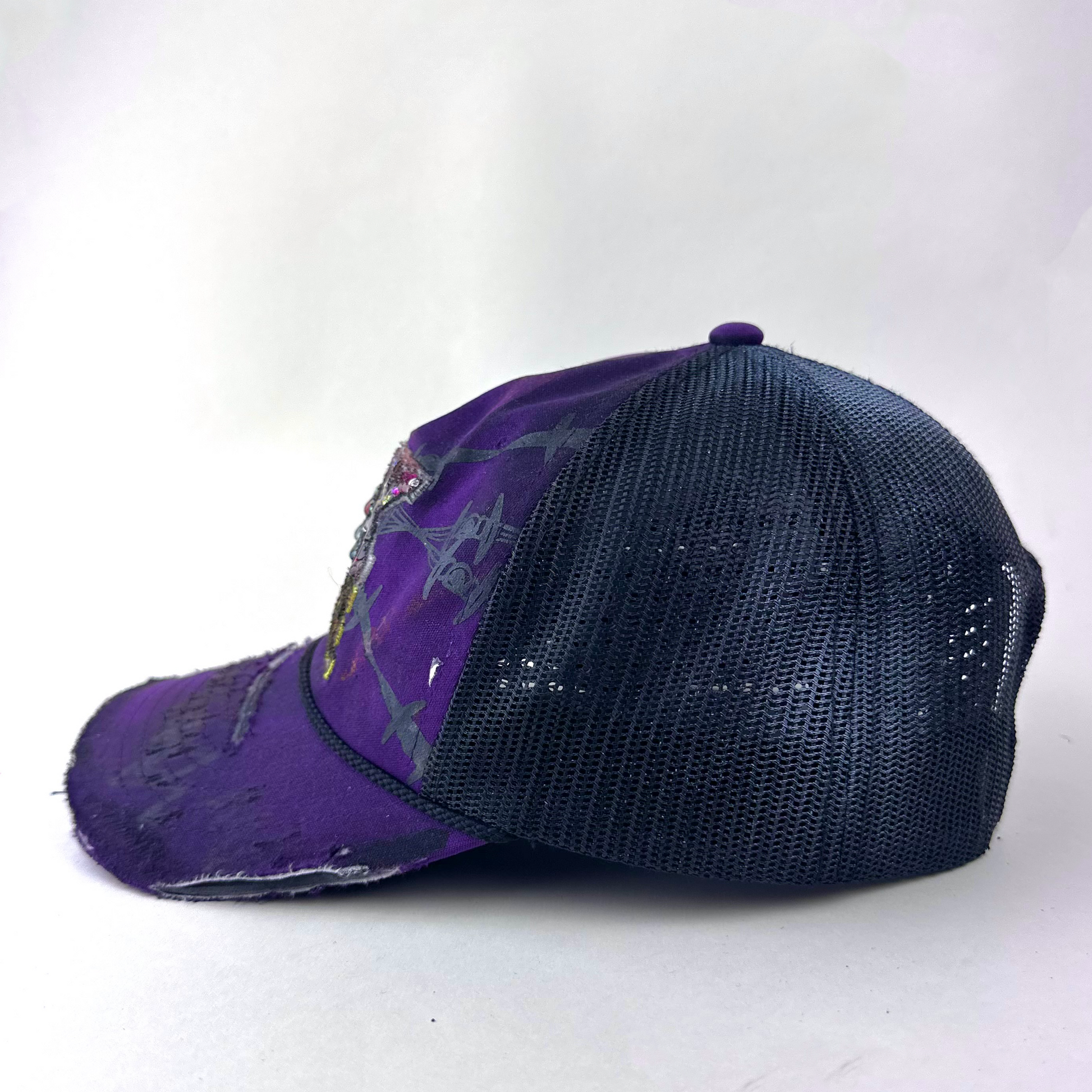 Left side detail of ASTROBOI* x Fox Racing 'Barbed Wire' showing deconstructed visor detail and multicolored rhinestone embellishment on purple hat.